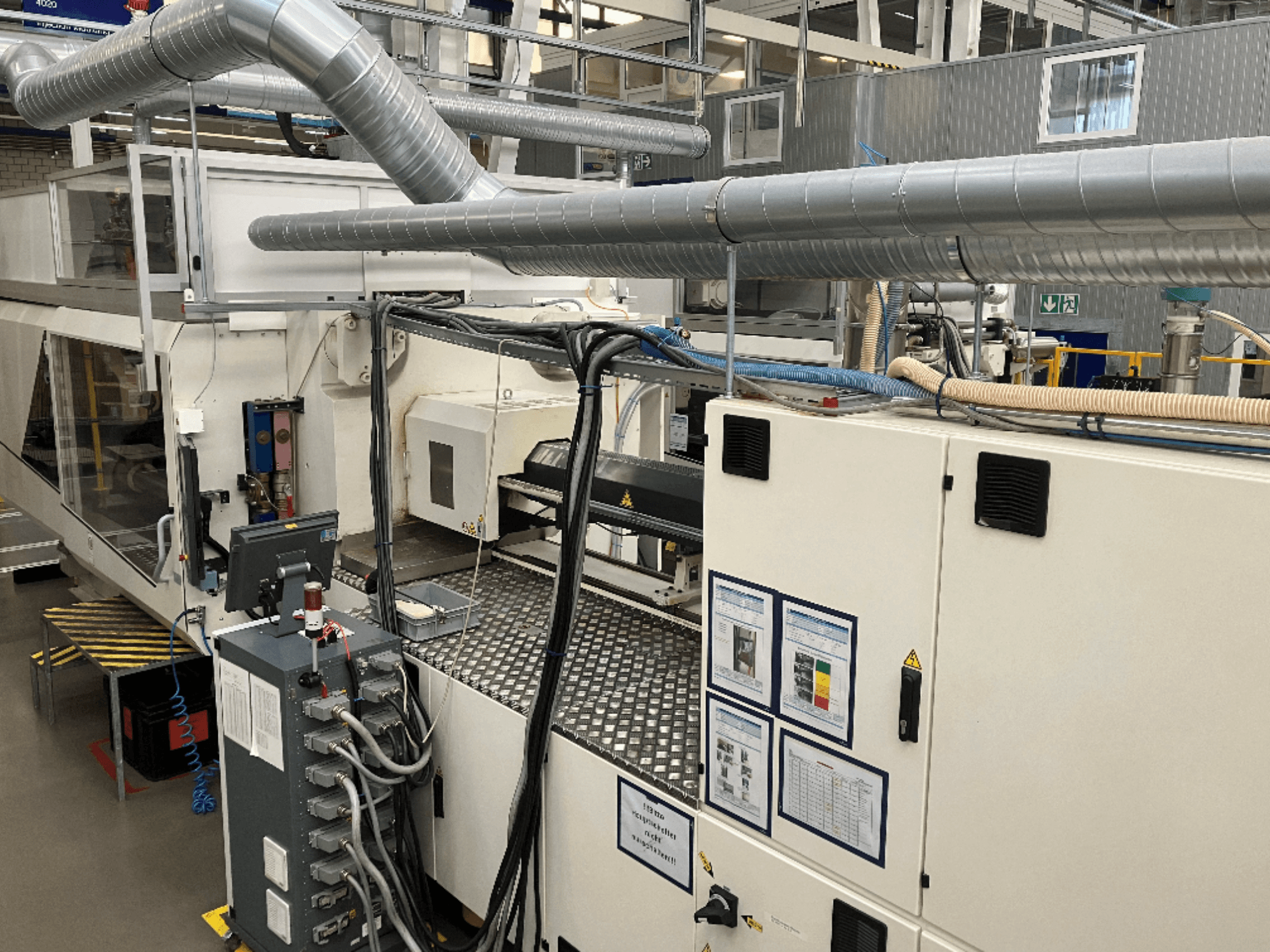 Průmyslové stroje s rozsáhlým potrubím, ovládacím panelem a návody k obsluze, pohled shora dolů.