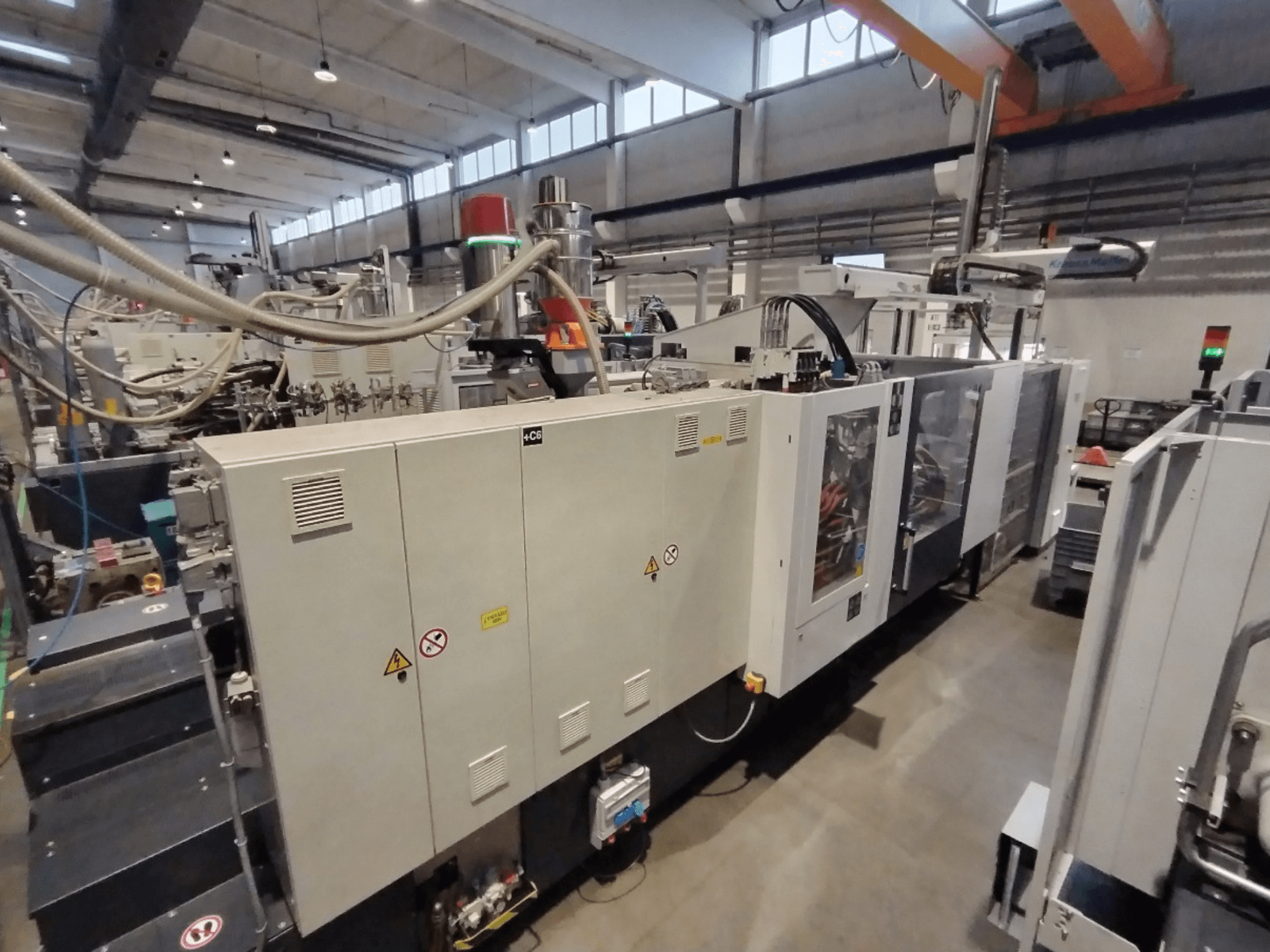 Průmyslový vstřikovací stroj zobrazený z bočního pohledu, s ovládacím panelem a bezpečnostními upozorněními. Značka: Neznámá značka.