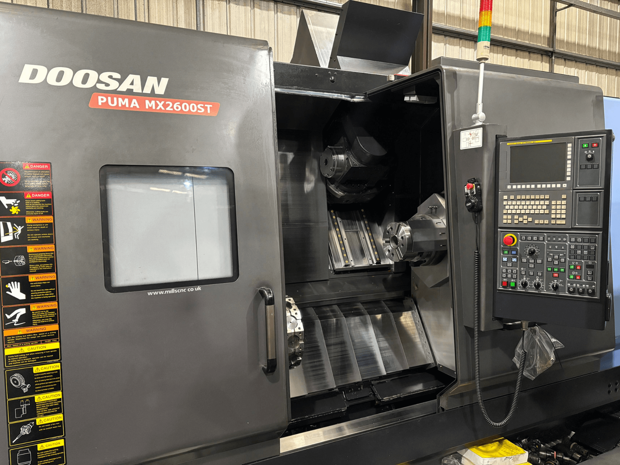 CNC soustruh Doosan PUMA MX2600ST, pohled zepředu, zobrazující ovládací panel, vřeteno a obráběcí prostor s viditelnými bezpečnostními upozorněními.