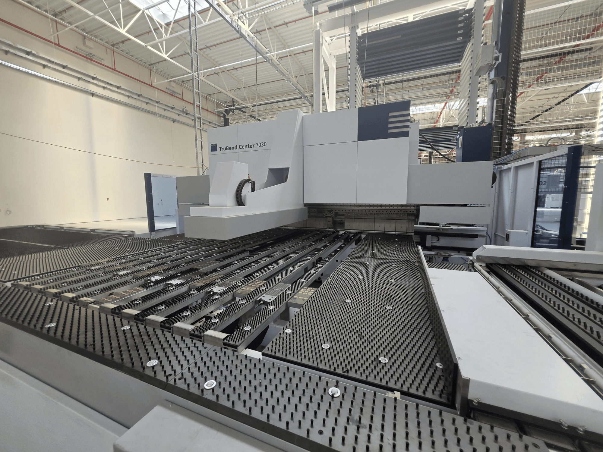 Ohýbačka TRUMPF TruBend Center 7030 v továrním prostředí, pohled zepředu znázorňující složitou konstrukci pracovního stolu a ohýbacího ramene.