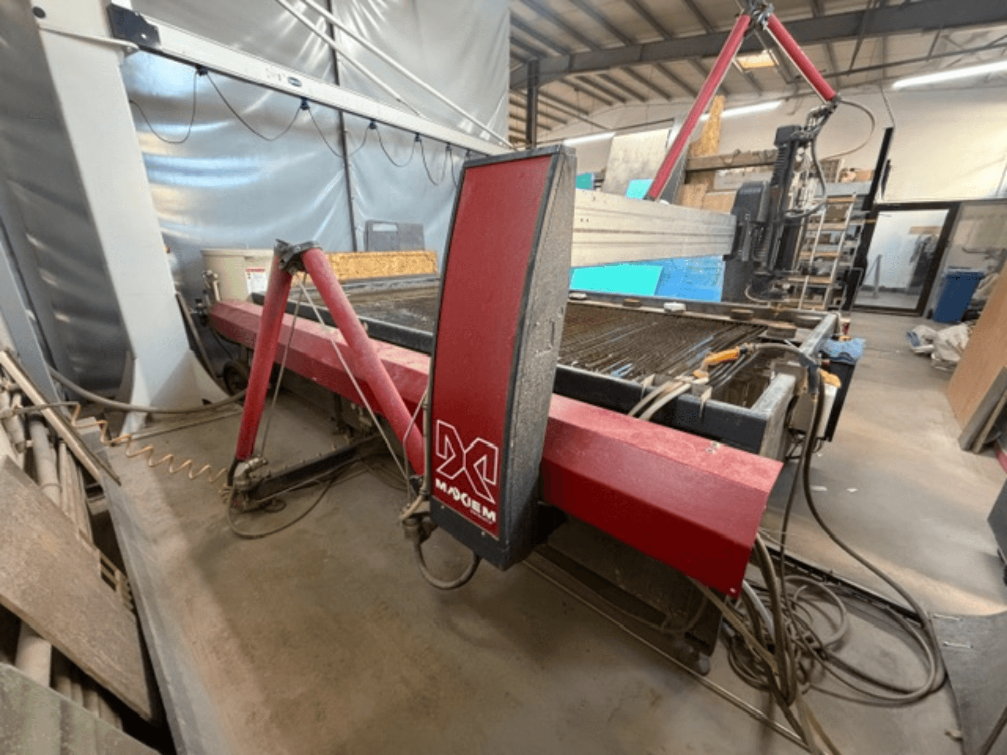 Červený stroj na řezání vodním paprskem značky X, pohled z boku, na kterém jsou vidět mechanické součásti a detaily potrubí.