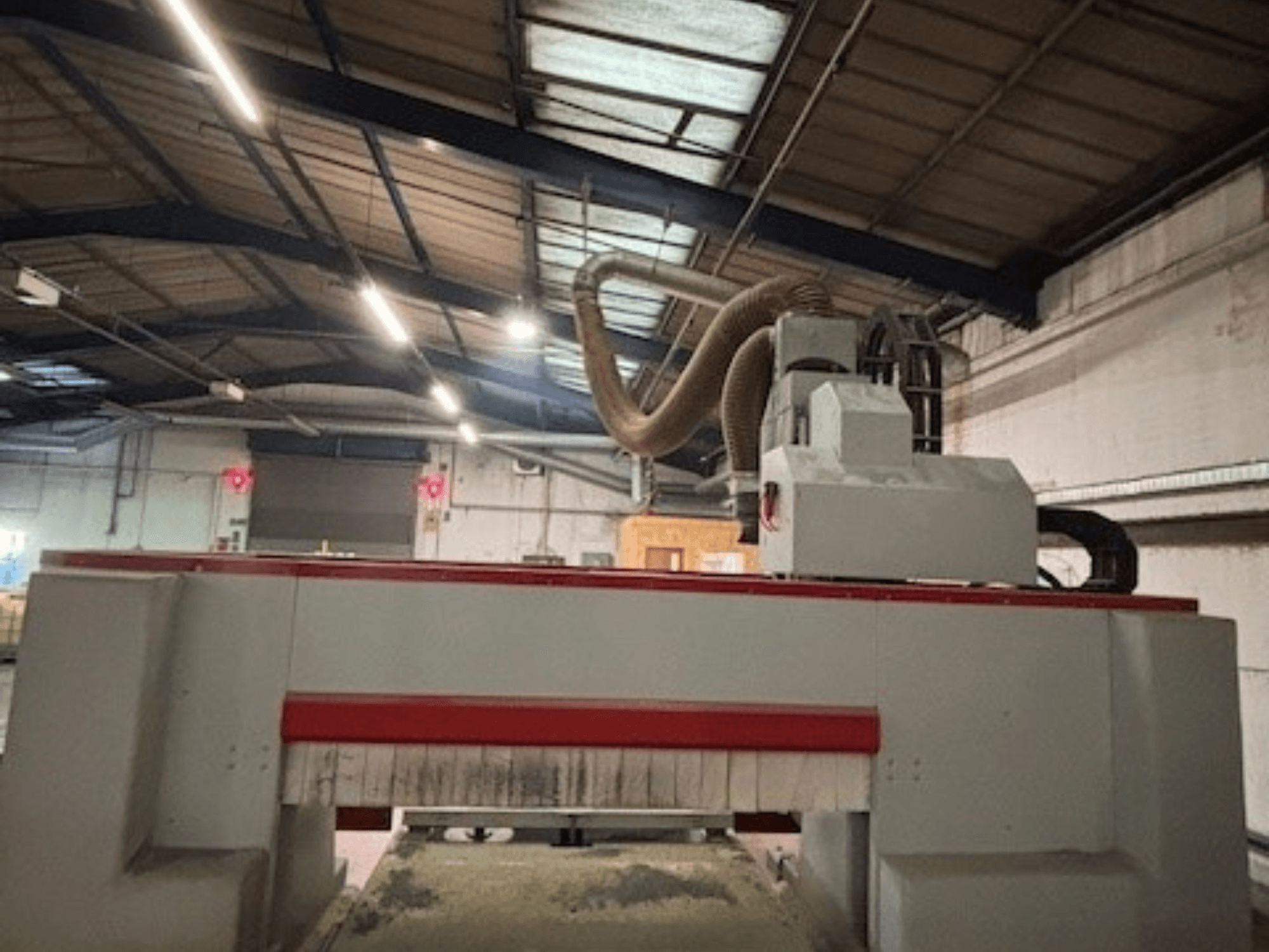 CNC frézka v dílně, boční pohled se zvýrazněným červeným a šedým provedením, připojený systém odsávání prachu.