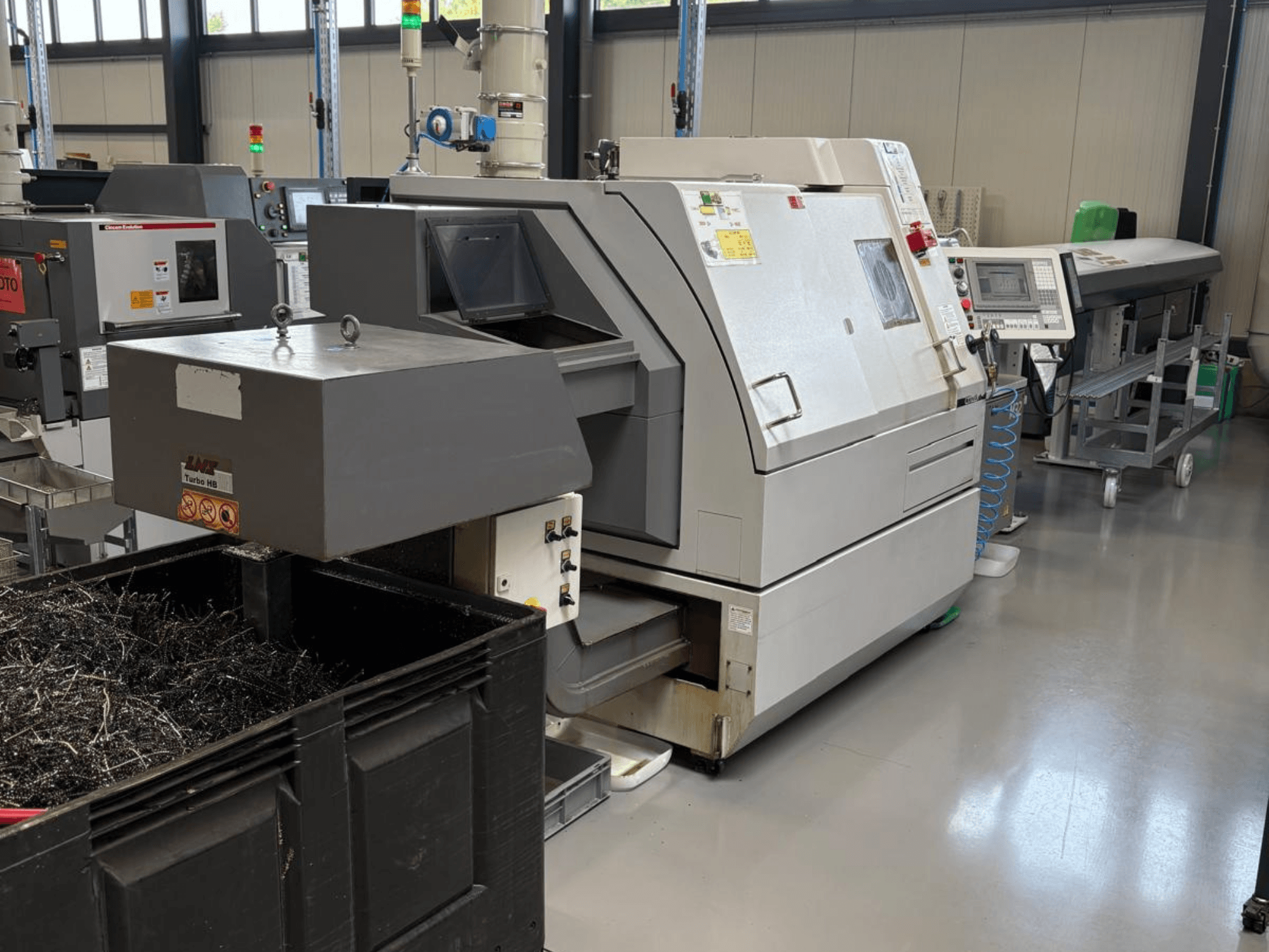 Průmyslový stroj LTA Turbo H8, boční pohled, s velkou nádobou na kovové hobliny a ovládacím panelem v továrním prostředí.