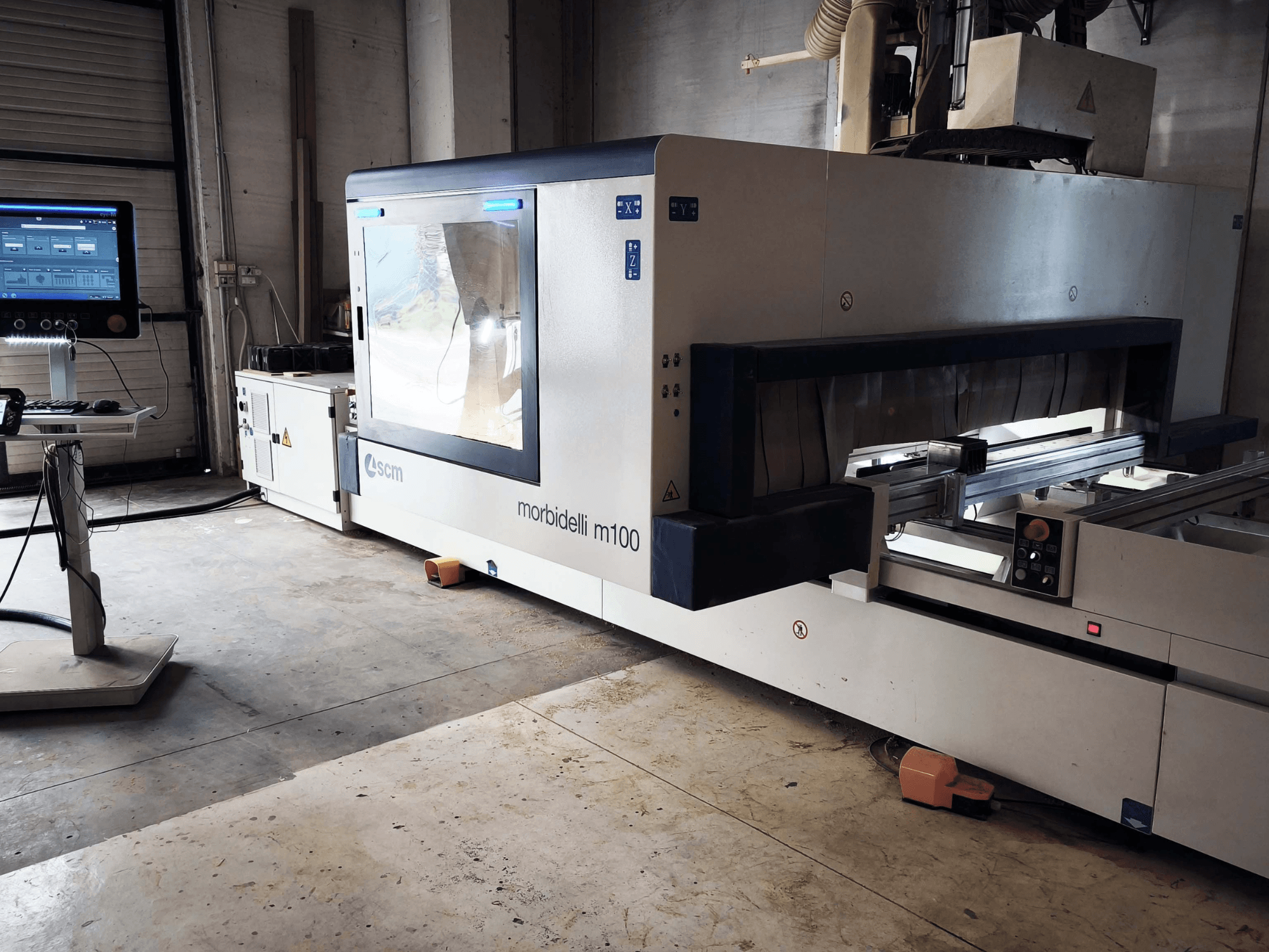 CNC centrum pro obrábění dřeva SCM Morbidelli M 100 v bočním pohledu, na kterém je vidět ovládací panel, pracovní prostor a bezpečnostní prvky.