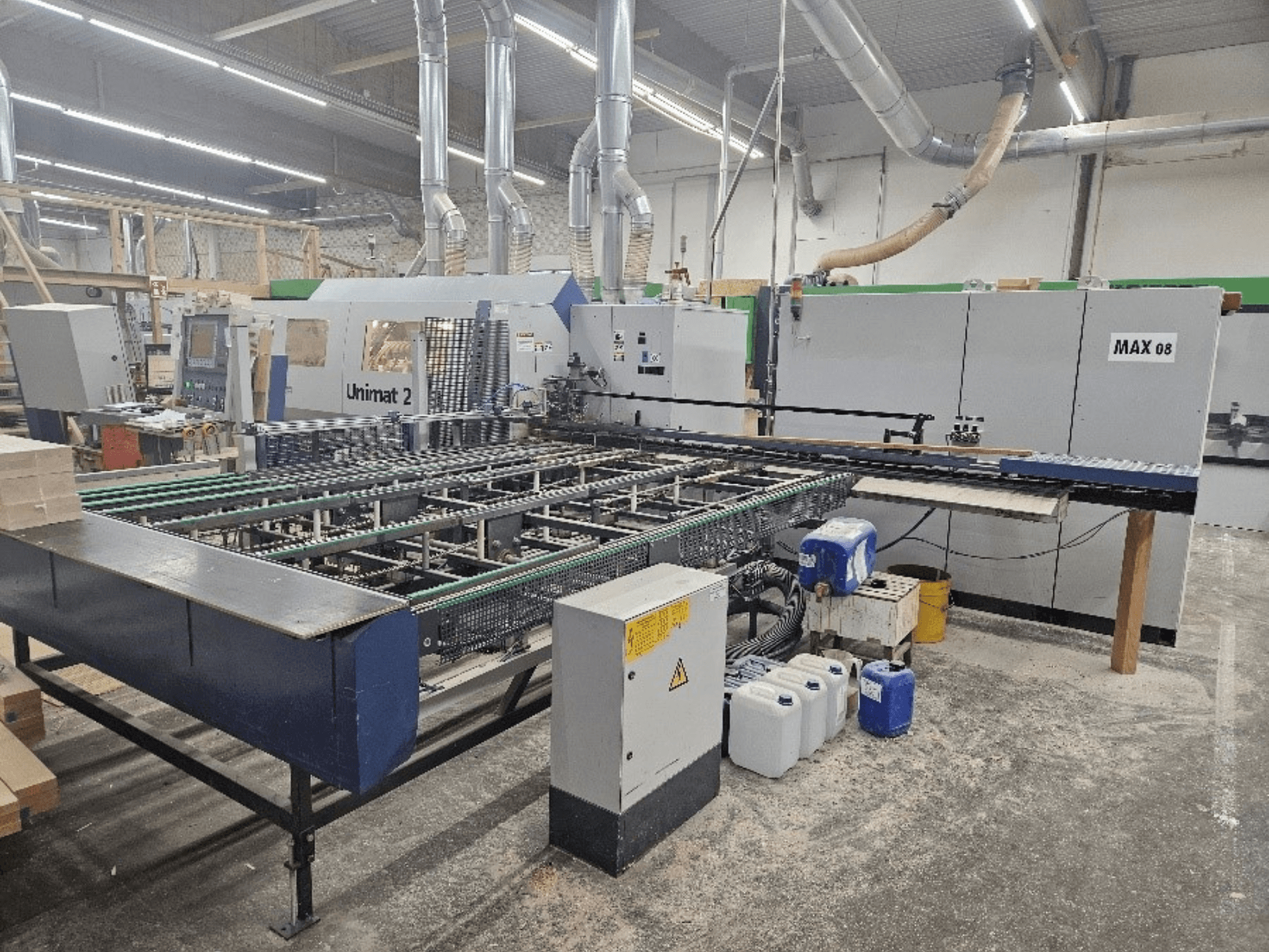 Boční pohled na stroj Unimat 2 CNC v dílně, s dopravníkovými pásy a technickými komponenty s viditelnou jednotkou Max 08.