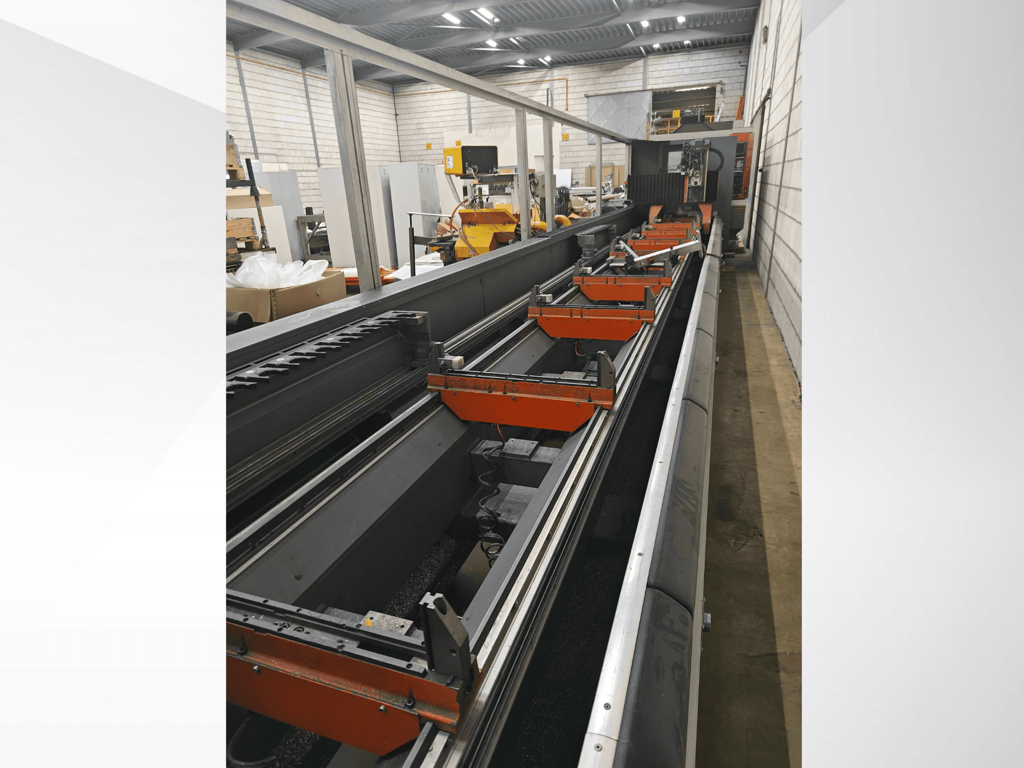 Boční pohled na průmyslový CNC stroj s lineárními lištami, oranžovými svorkami a přesnými součástkami ve skladu.