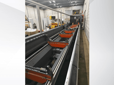 Boční pohled na průmyslový CNC stroj s lineárními lištami, oranžovými svorkami a přesnými součástkami ve skladu.