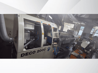 Stroj DECO 2000 CNC v dílně, pohled zepředu, ovládací prvky a dlouhé nastavení obrobku vpravo.