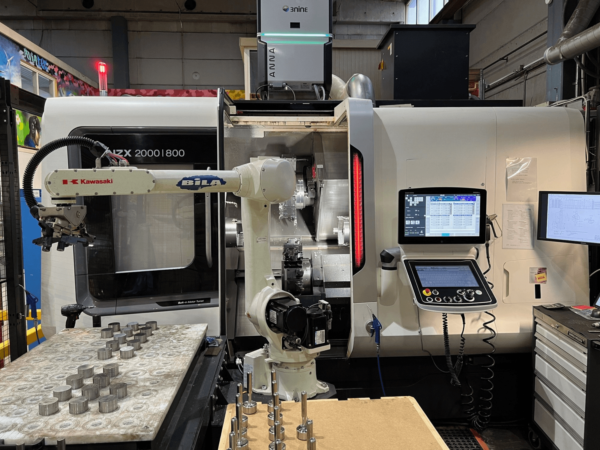 Horizontální soustruh DMG MORI NZX 2000/800SY v dílně, na snímku je vidět robotické rameno Kawasaki a ovládací prvky.