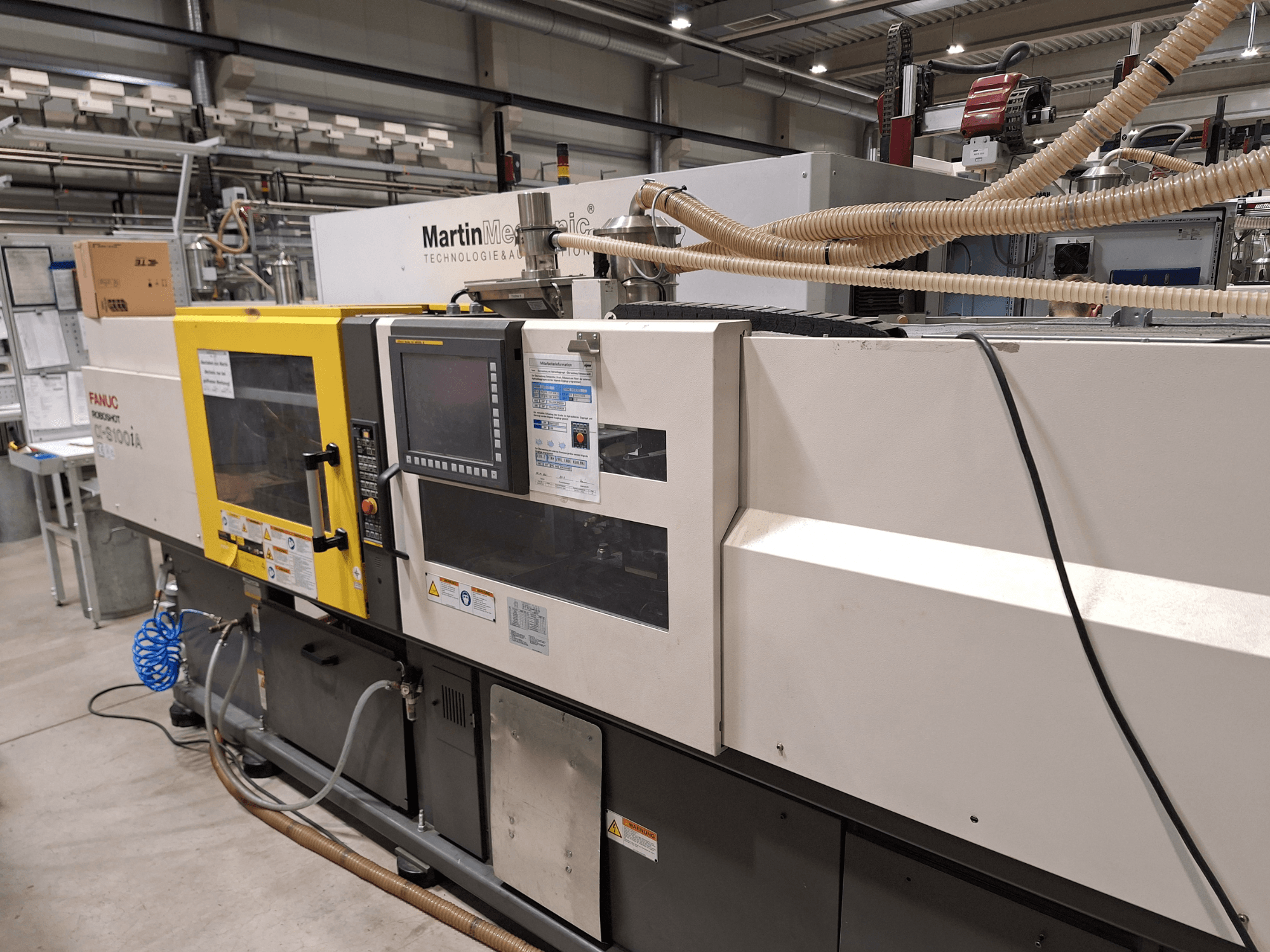 Elektrický vstřikovací stroj FANUC Roboshot S100iA, boční pohled, vybavený dotykovou obrazovkou a bezpečnostními štítky.