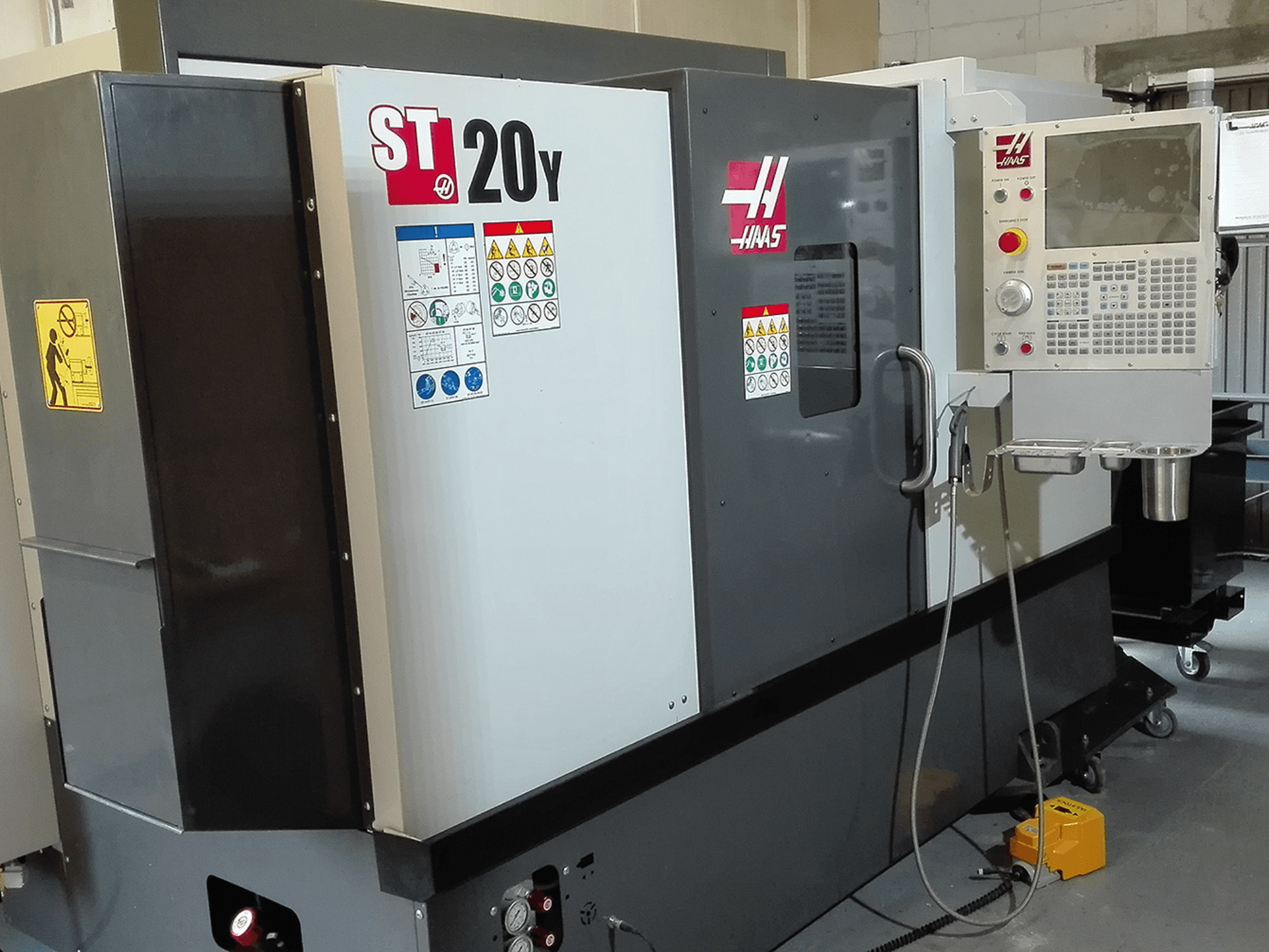 CNC soustruh Haas ST20Y v čelním pohledu, s ovládacím panelem, bezpečnostními štítky a chladicím systémem.