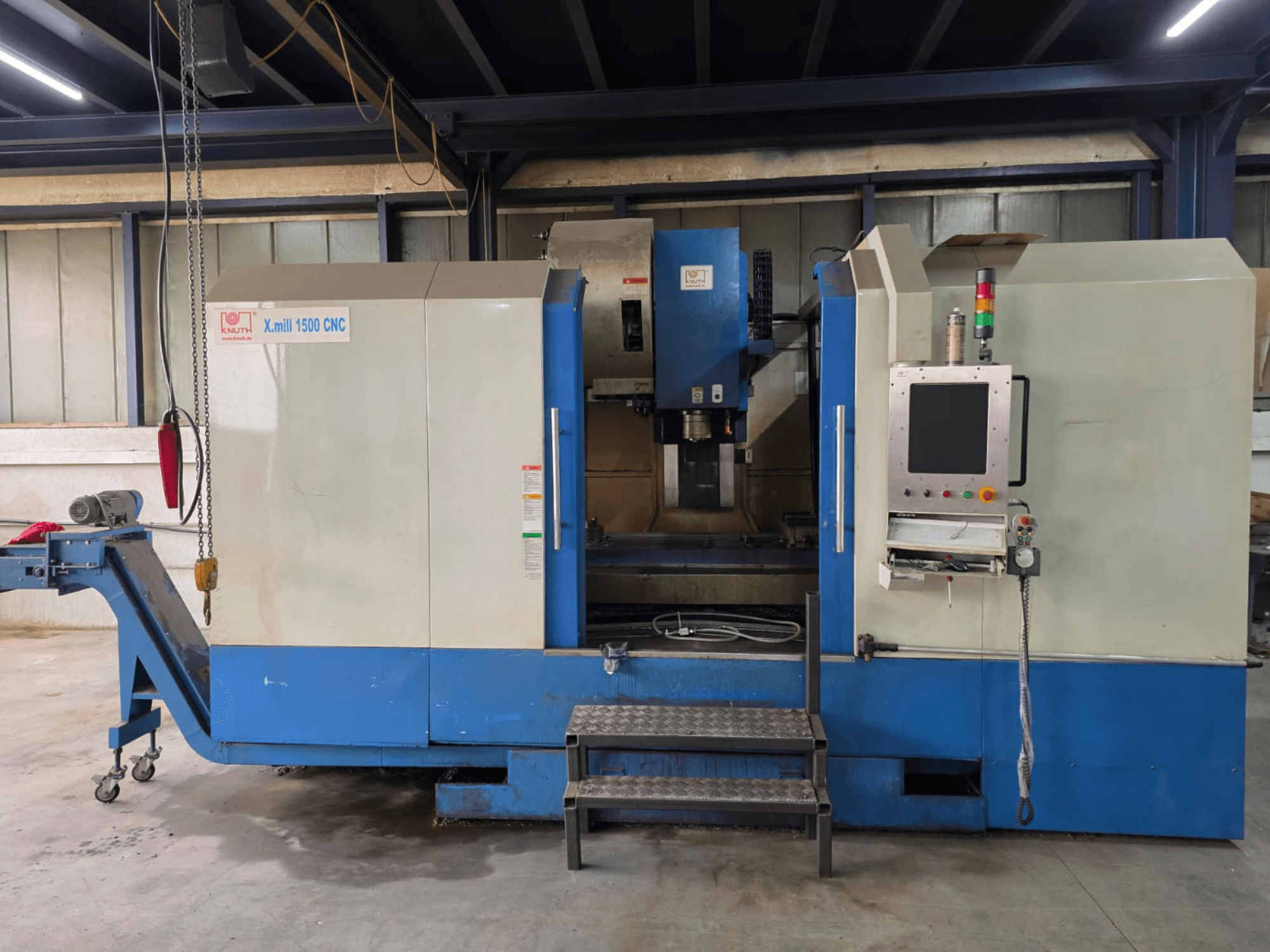 Vertikální obráběcí centrum KNUTH X-MILL 1500 s řízením CNC, pohled z boku; na obrázku je vidět ovládací panel, schody a výstupní dopravník.