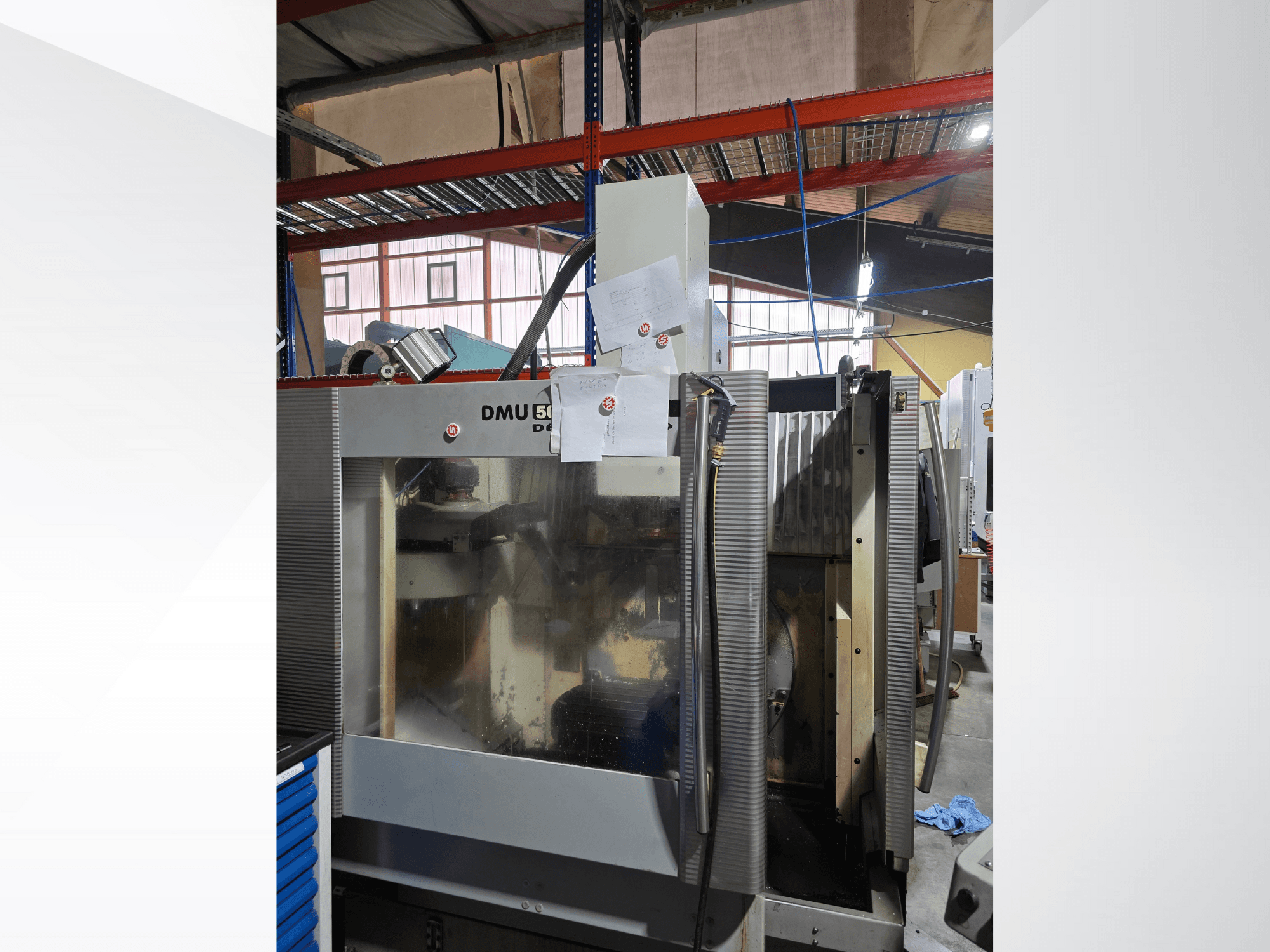 Tříosé CNC obráběcí centrum DMU 50 v dílně, zobrazené zepředu, s provozními komponenty a přiloženými dokumenty.