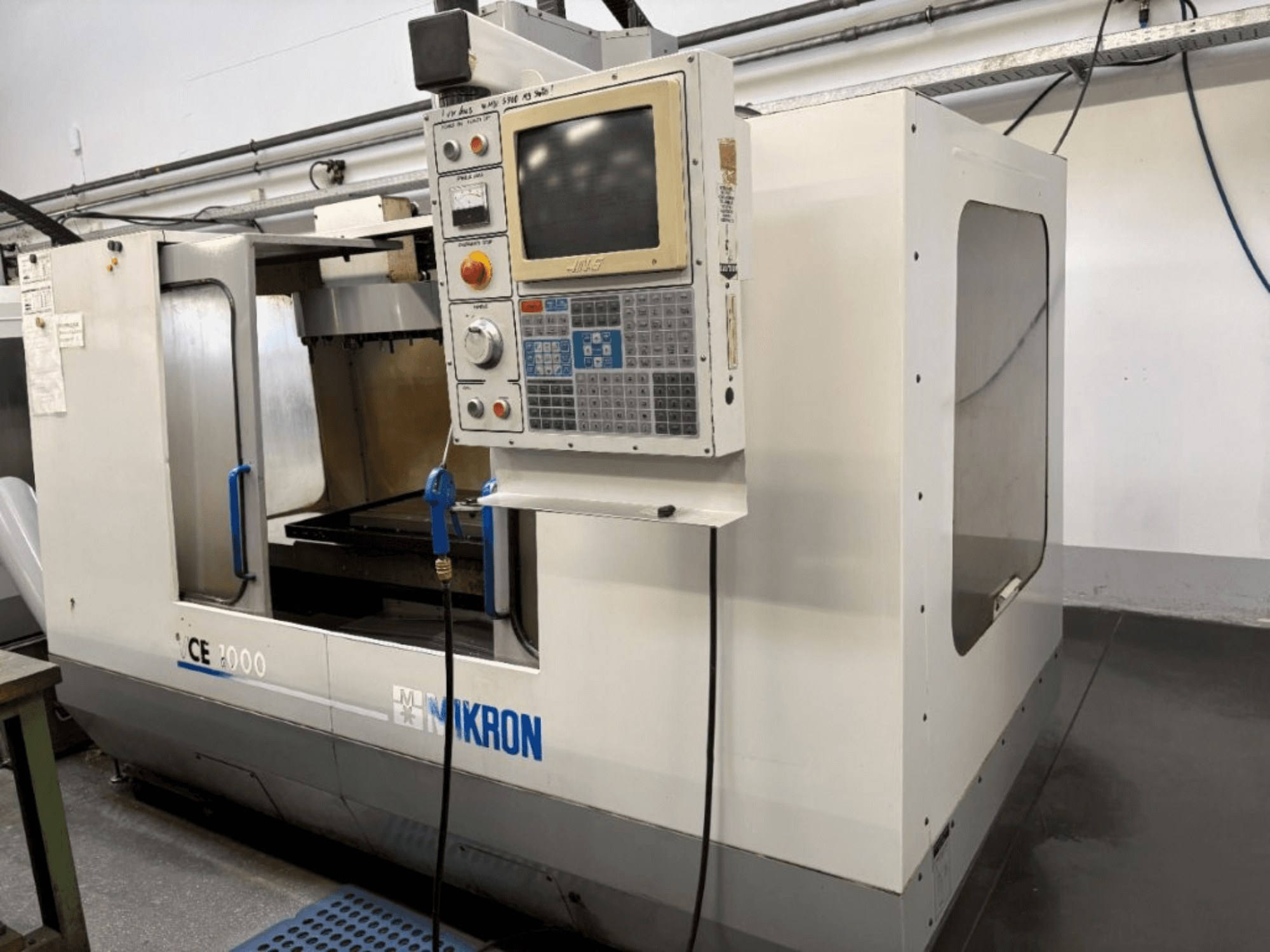 Stroj Mikron CE 2000 CNC, pohled zepředu; ovládací panel s tlačítky a obrazovkou, stříbrný exteriér a pracovní plocha.