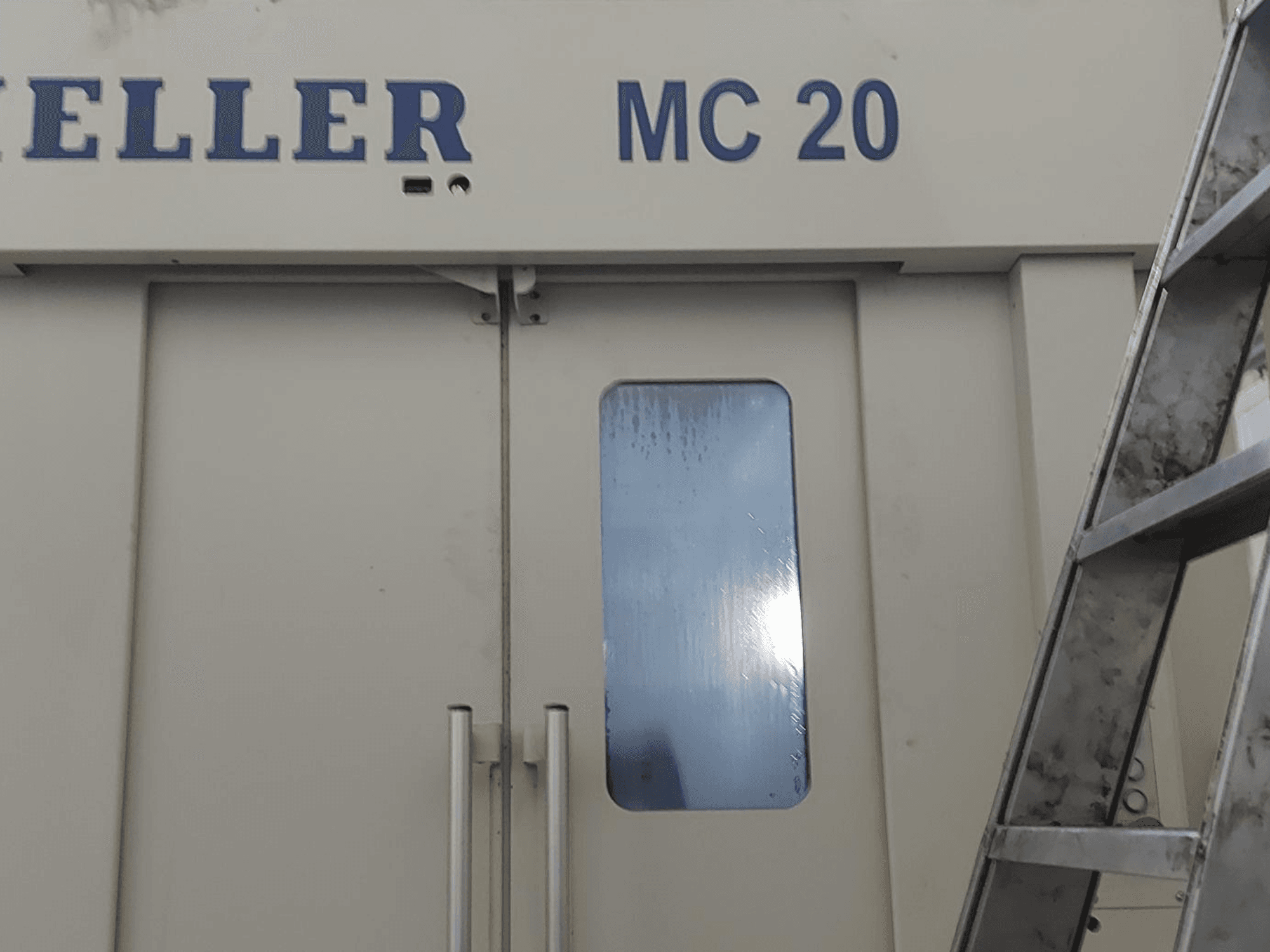Pohled zepředu na horizontální obráběcí centrum HELLER MC 20, na kterém jsou vidět kliky dveří a malé okénko. Žebřík na boku.