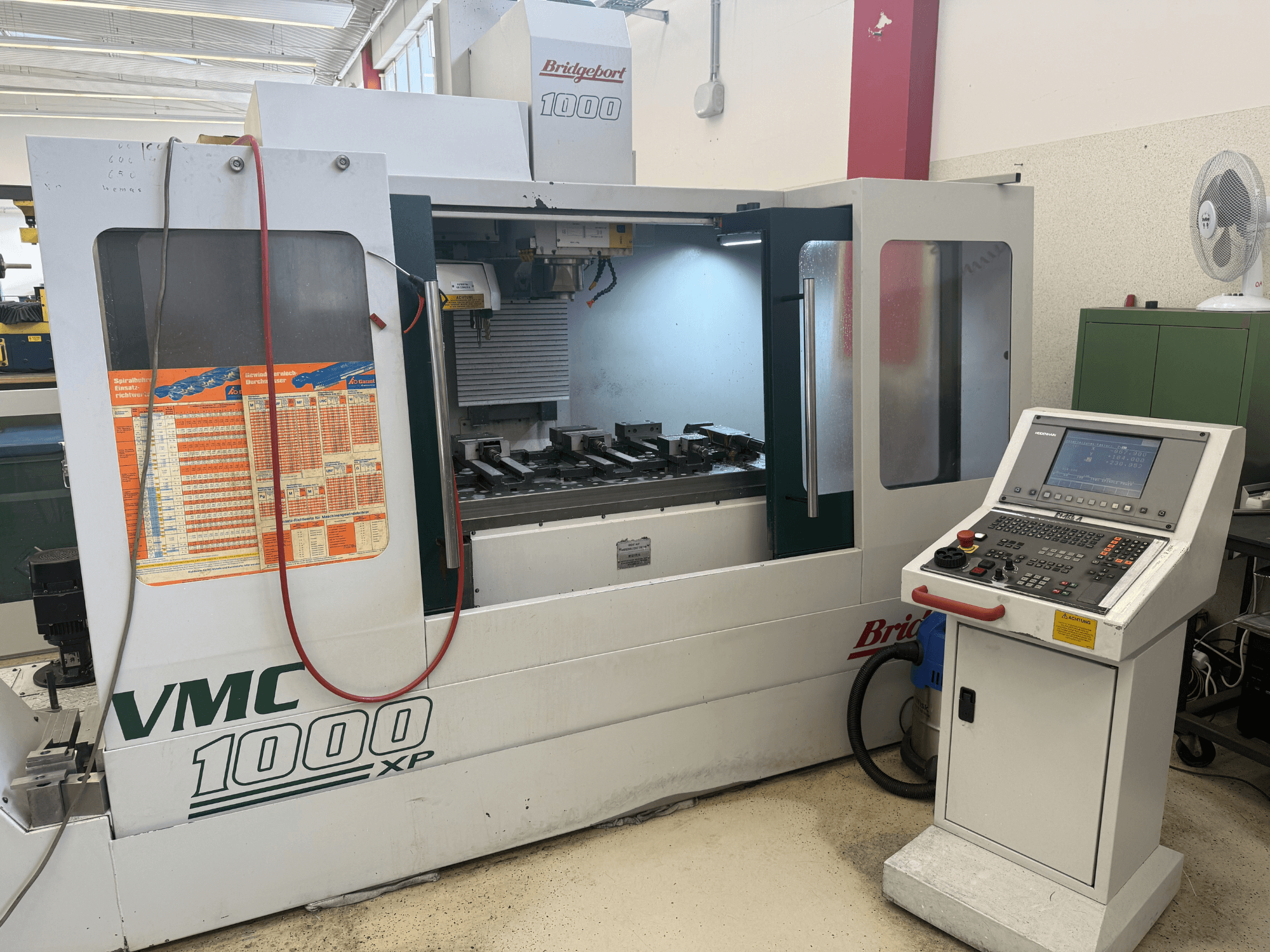 Pohled zepředu na vertikální obráběcí centrum Bridgeport VMC 1000 XP, na kterém jsou vidět ovládací prvky, pracovní prostor a upínací zařízení pro nástroje.