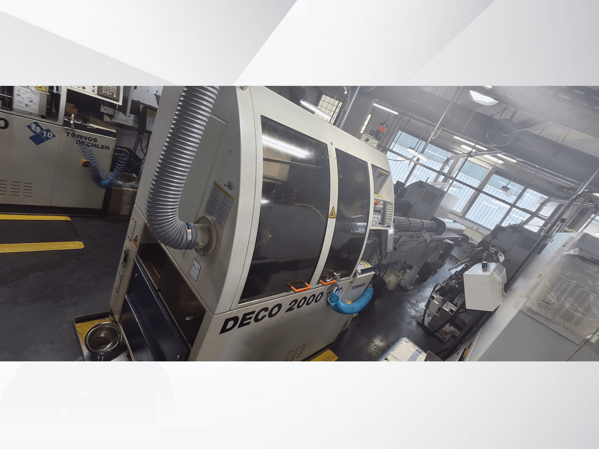 Stroj DECO 2000 CNC v dílně, pohled zepředu, s ventilační hadicí a ovládacím panelem, určený pro přesné obrábění.