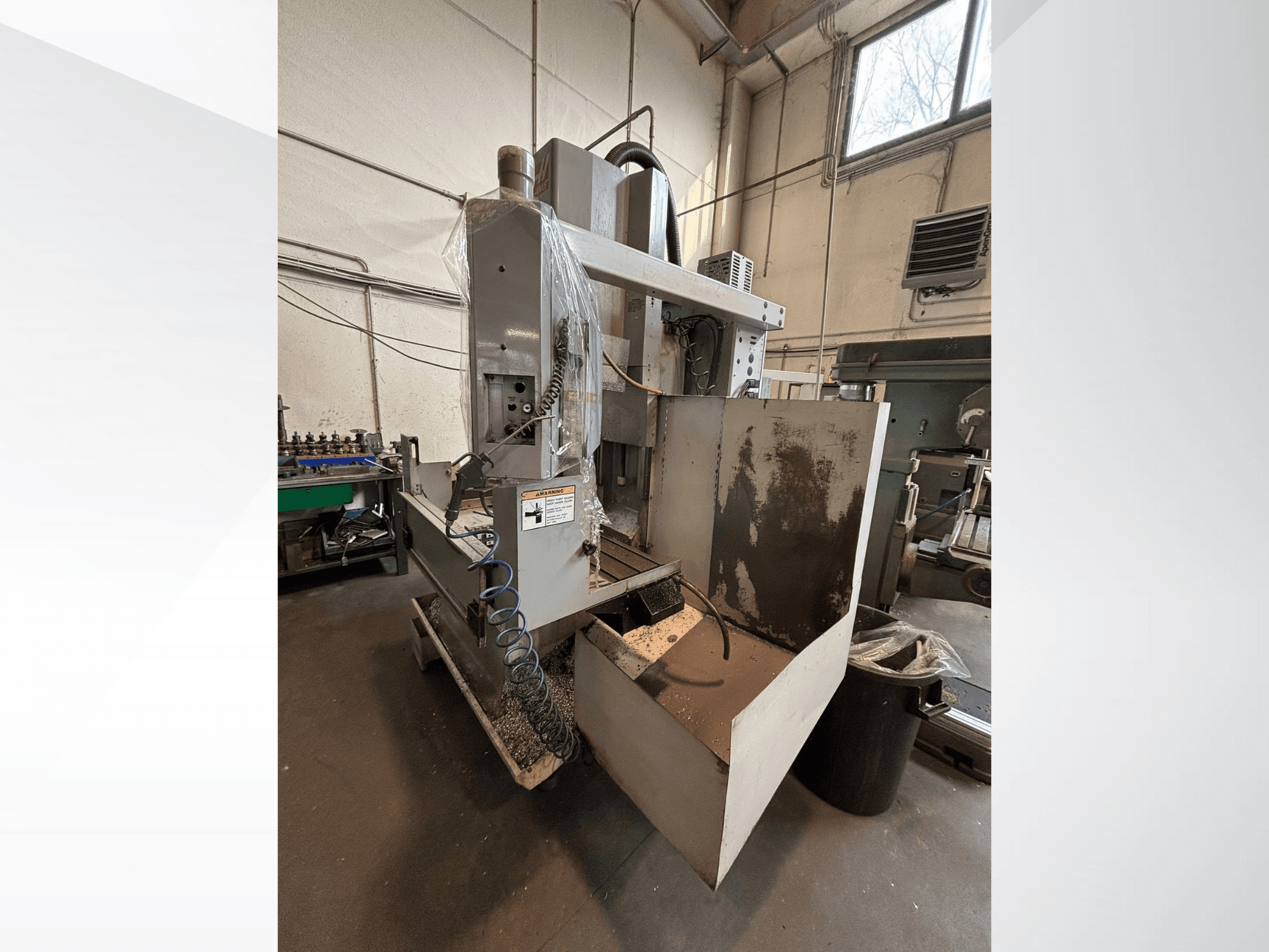 Vertikální frézka s ochranným krytem, boční pohled; včetně viditelné hadice chladicí kapaliny a ovládacího panelu. Ideální pro obrábění.