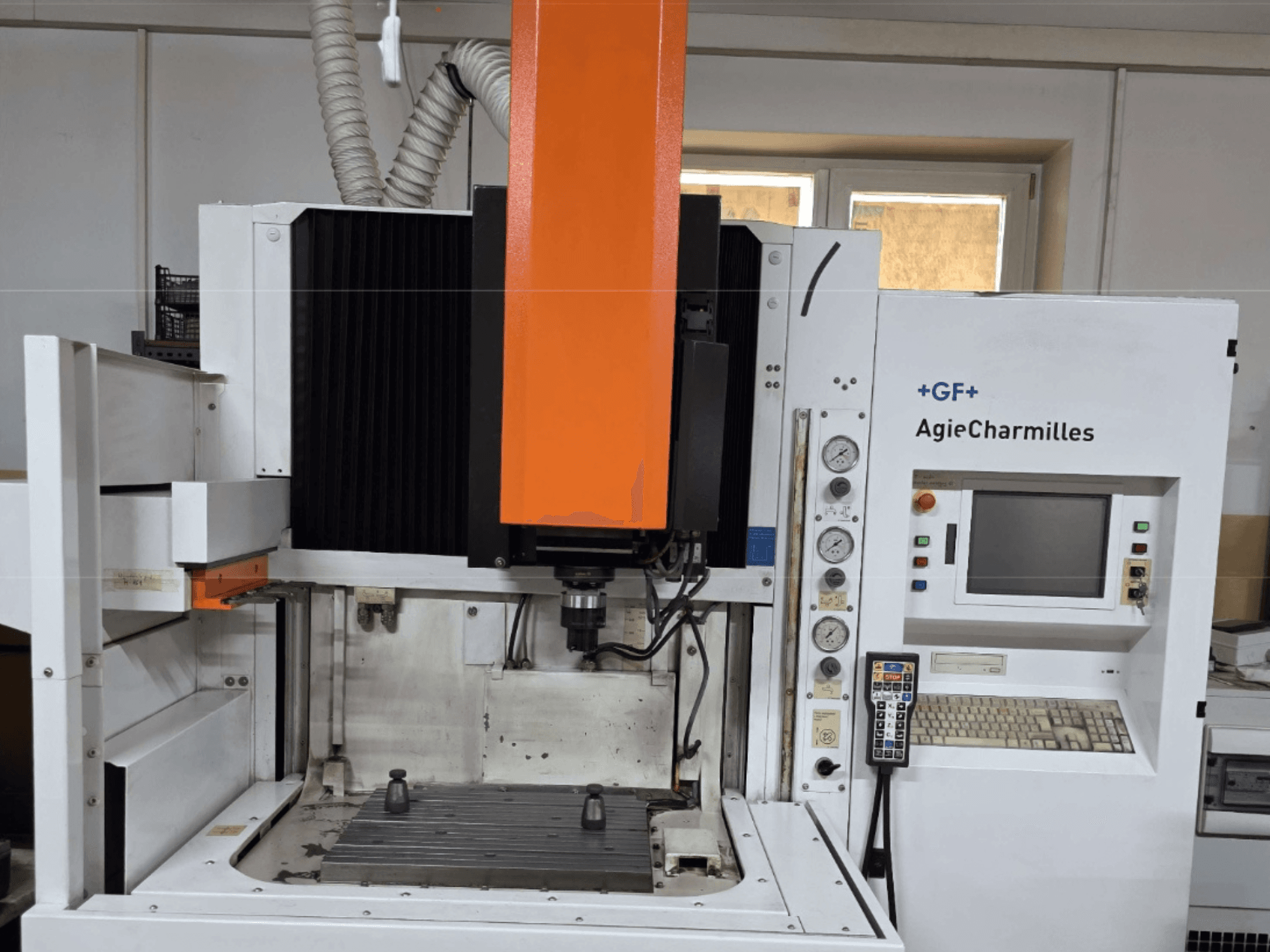 Obráběcí centrum AgieCharmilles v čelním pohledu s velkým oranžovým vřetenem, ovládacím panelem a viditelným pracovním stolem.