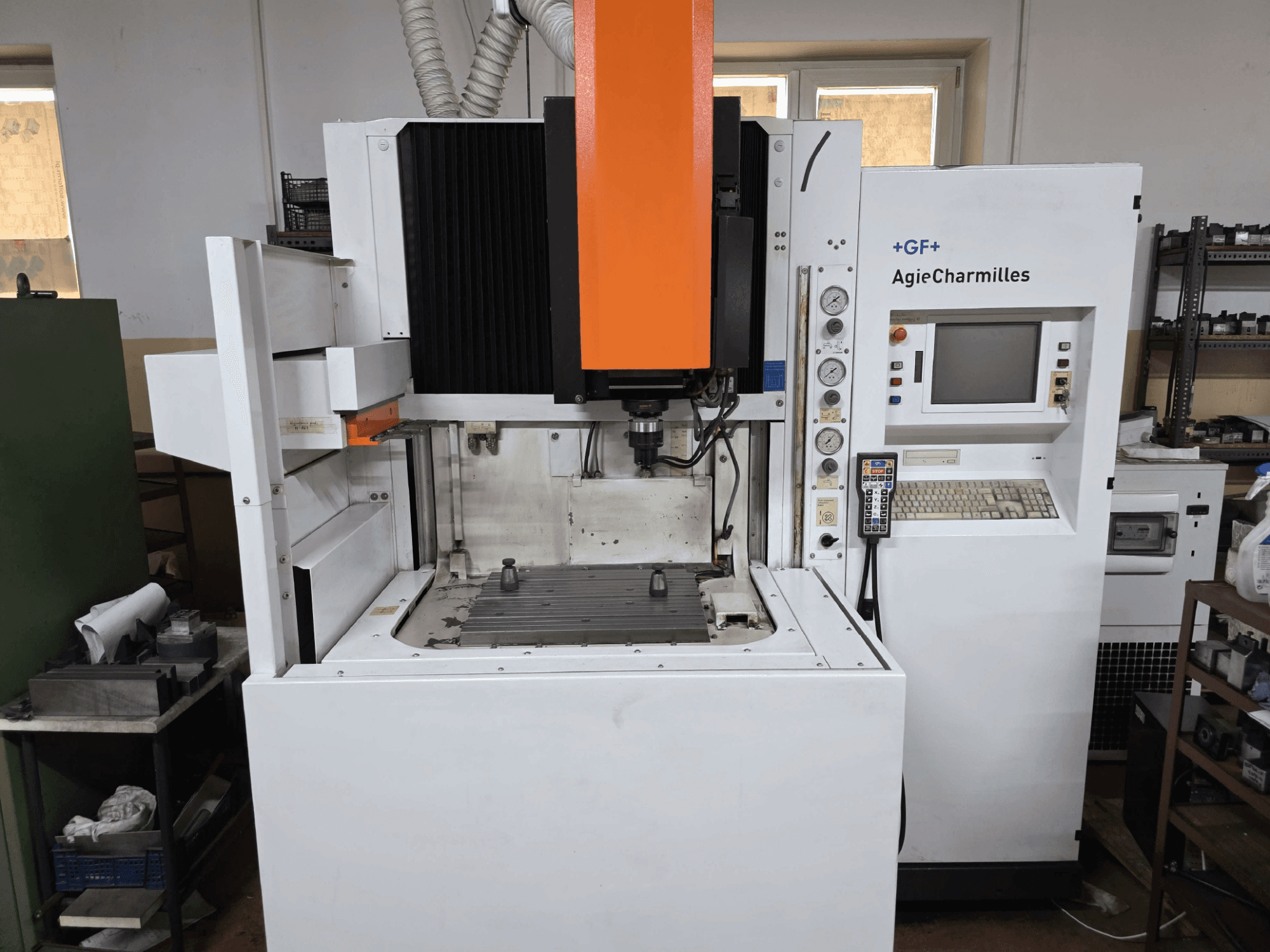 CNC stroj GF AgieCharmilles, čelní pohled s výrazným oranžovým vřetenem, digitálním ovládacím panelem a namontovaným vrtacím stolem.