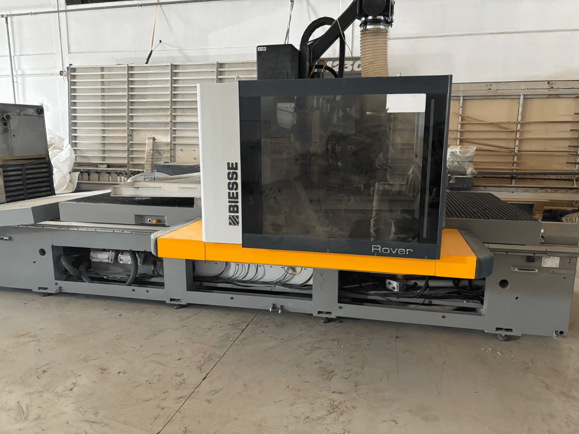 CNC obráběcí centrum Biesse Rover, pohled zepředu, s velkým ovládacím panelem, žlutými akcenty a odkrytými mechanickými součástmi.