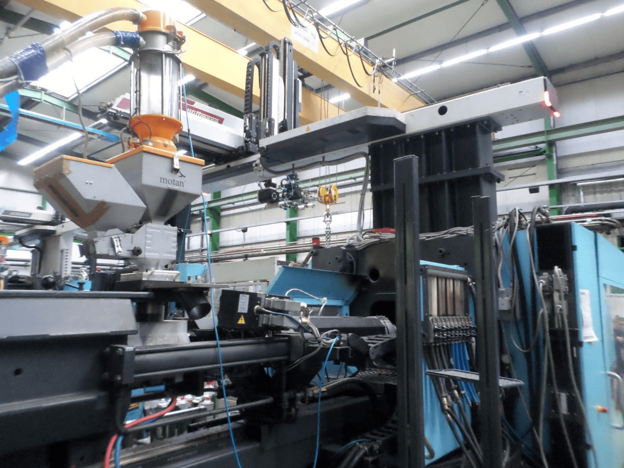 Hydraulický vstřikovací stroj DEMAG D 1300, boční pohled, znázorňující zásobník, řídicí jednotku a přípojky v továrním nastavení.