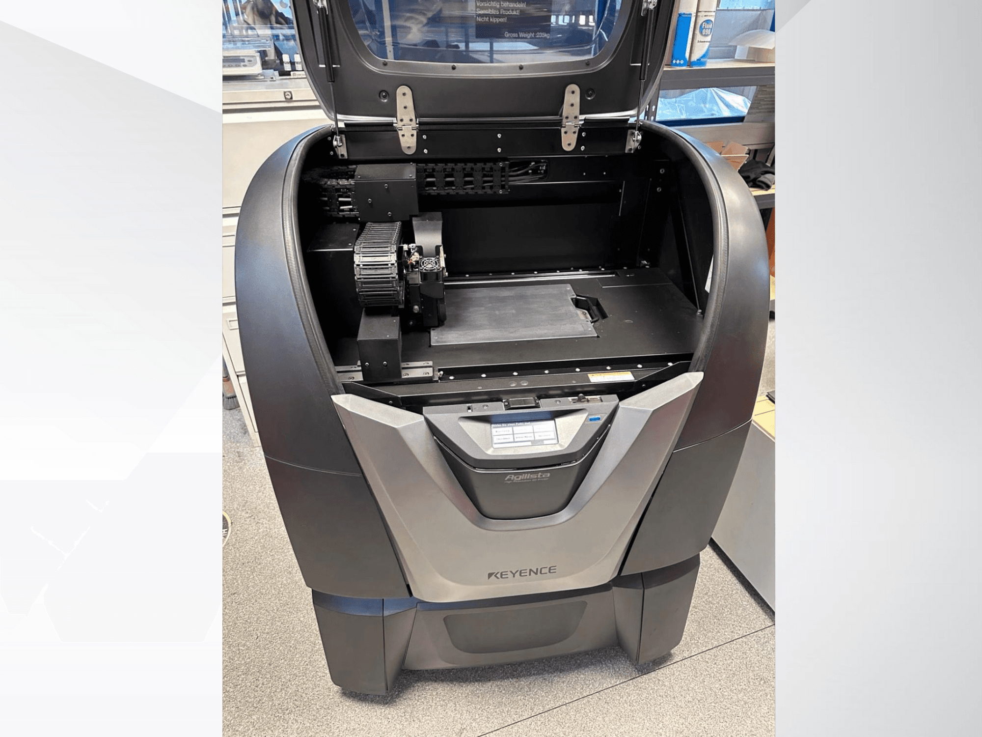 3D tiskárna KEYENCE Agilista, pohled zepředu, odhaluje otevřenou horní část, velkou stavební platformu a vnitřní mechanické součásti.
