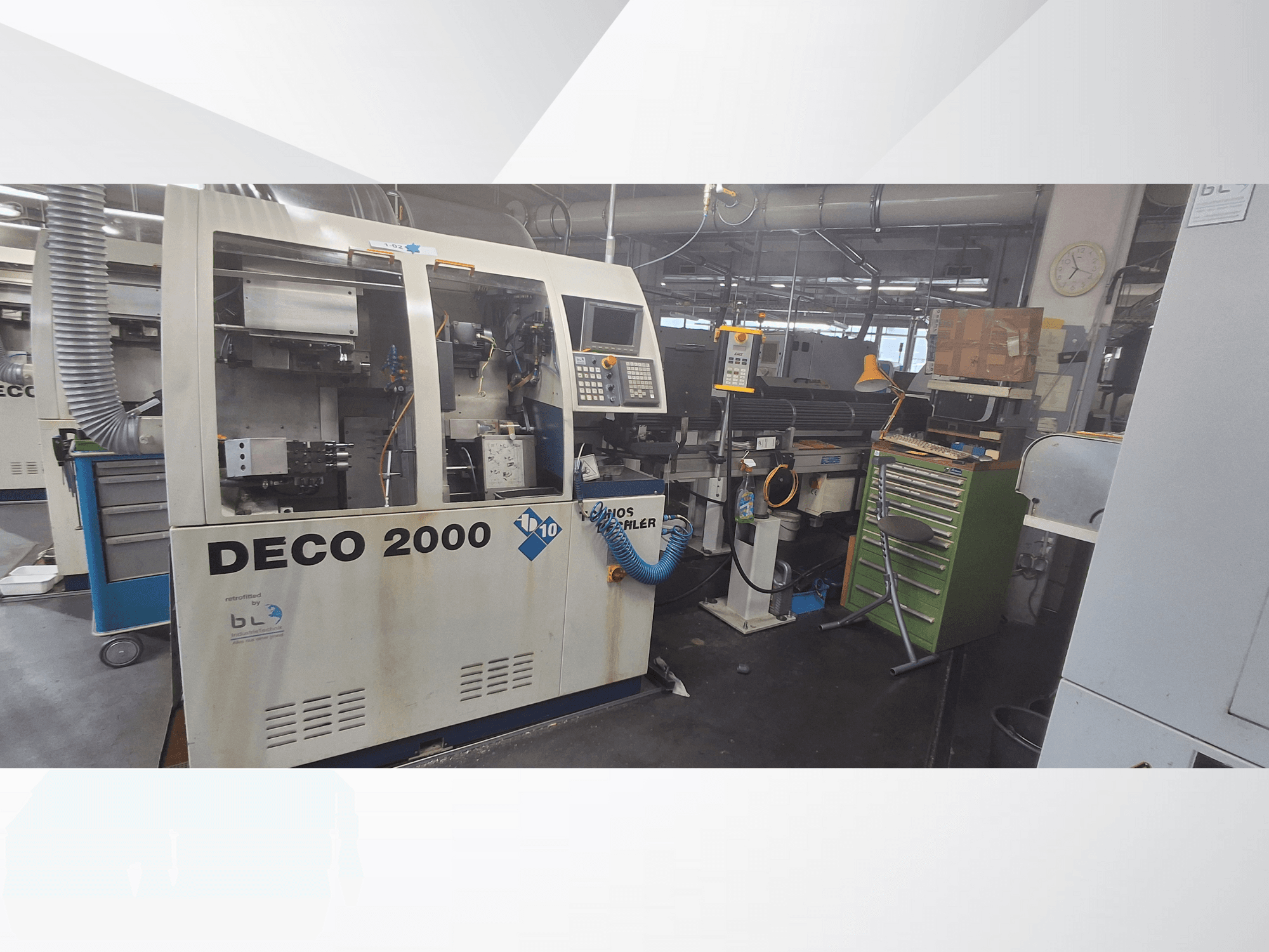 Stroj DECO 2000 při pohledu zepředu, s ovládacím panelem, trubkami a přeplněným pracovním prostorem s nářadím a krabicemi.