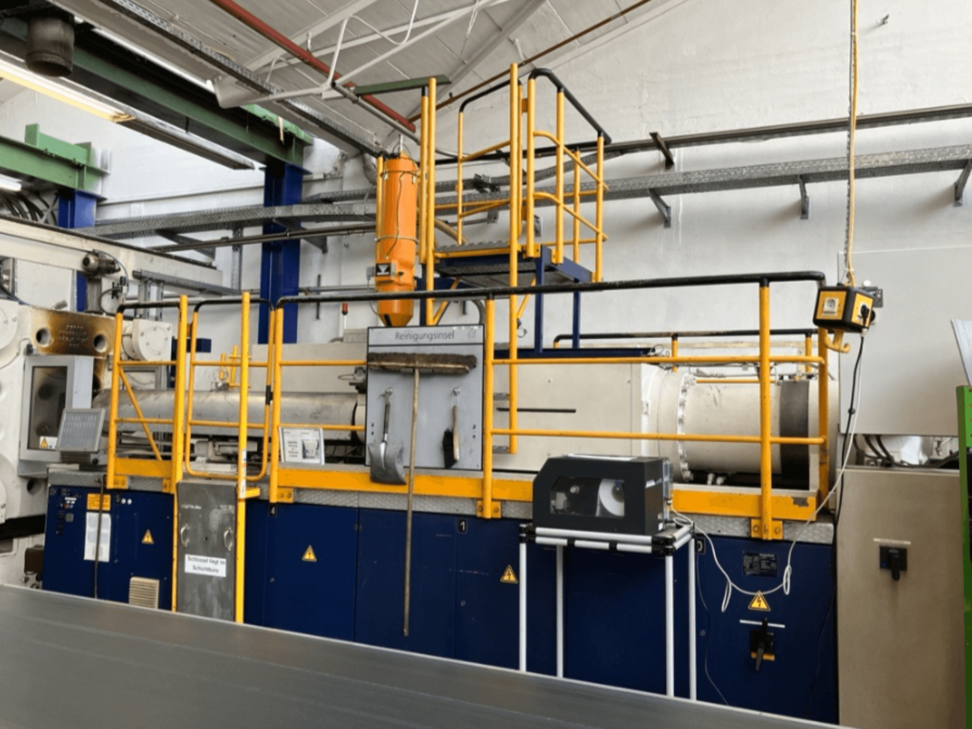 Hydraulický vstřikovací stroj Krauss Maffei 1000-8000 M, boční pohled s viditelným bezpečnostním zábradlím a ovládacím panelem.