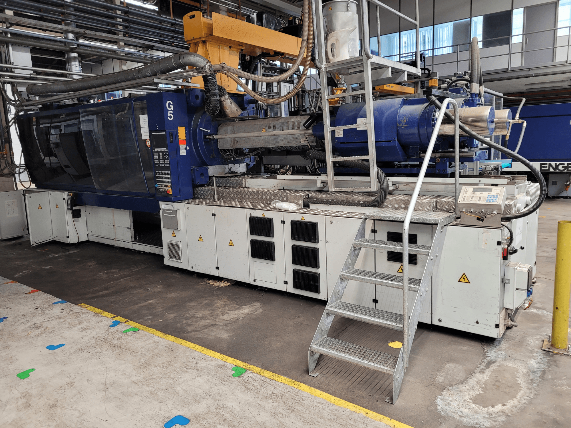 Vstřikovací stroj G5, boční pohled, s viditelným ovládacím panelem, žebříkem a pracovní plochou z nerezové oceli.