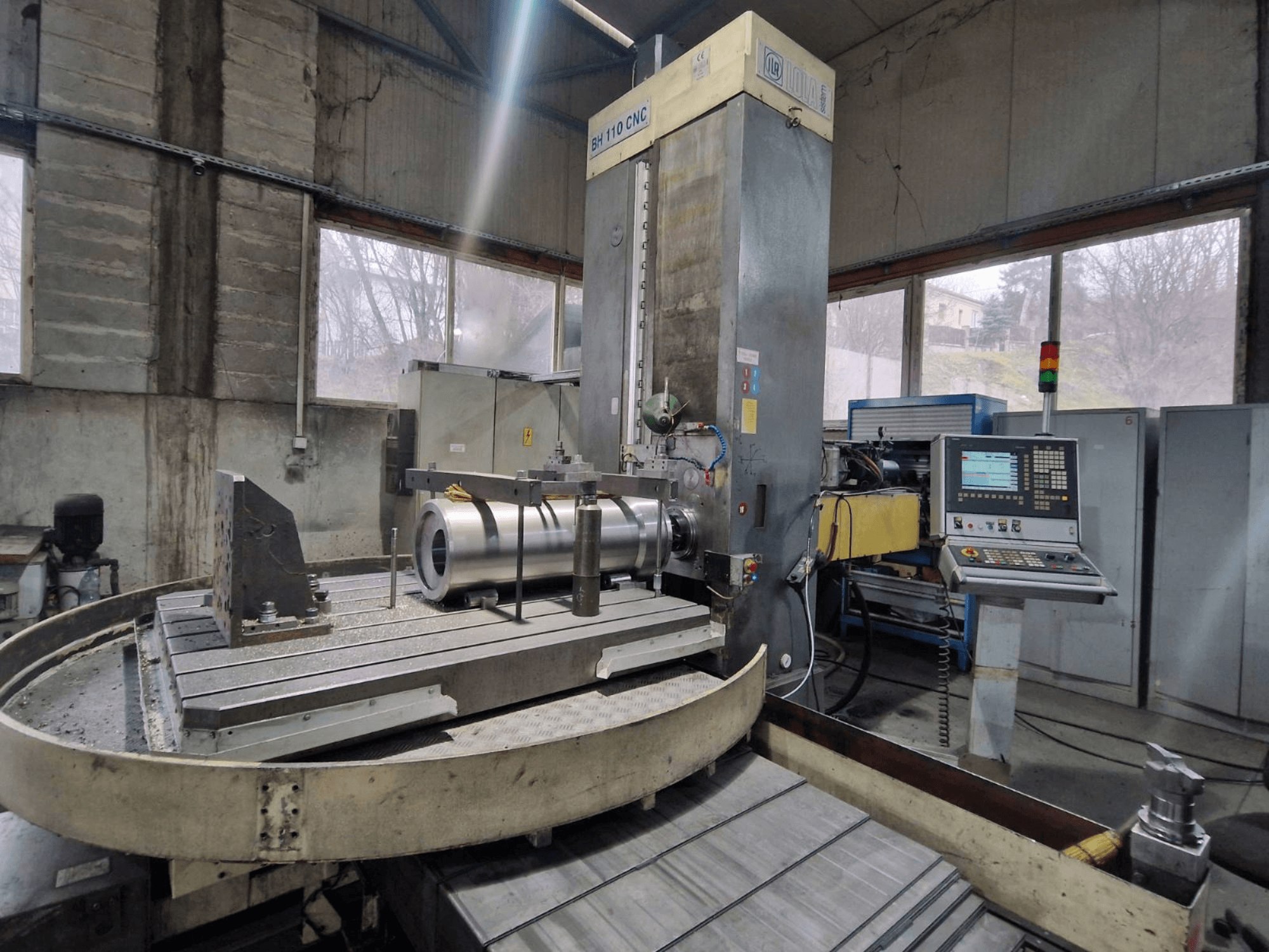 CNC vyvrtávačka LOLA BH 110 v dílně, pohled zepředu, kovový obrobek a ovládací panel.