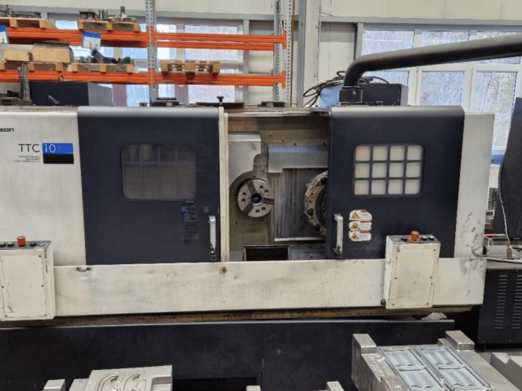 Pohled zepředu na soustruh TTC 10, zobrazující ovládací panel, viditelná sklíčidla a pracovní prostor s kovovými díly.
