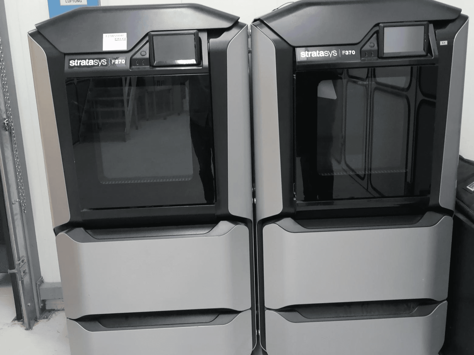 Duální plastové 3D tiskárny Stratasys F370 zobrazené v čelním pohledu, s elegantním černo-stříbrným designem a ovládacími obrazovkami.