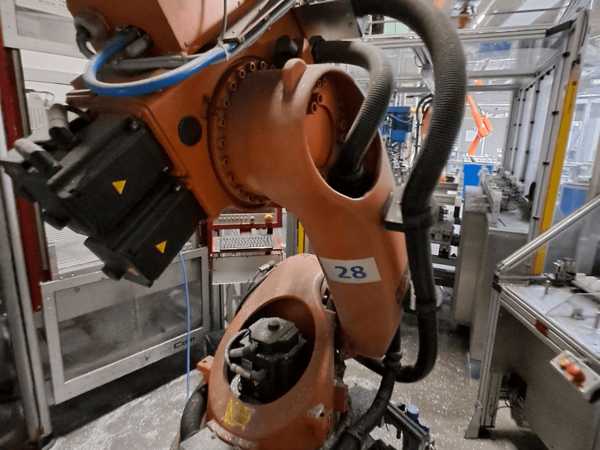 Detailní záběr robotického ramene KUKA KR30-3 s oranžovým tělem, označeného číslem 28, na kterém jsou z bočního pohledu vidět motory a kabeláž.