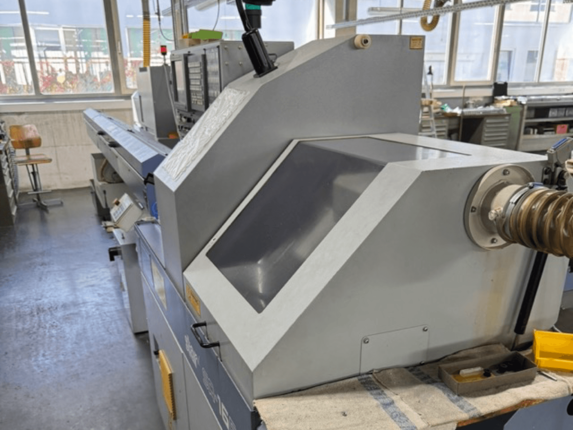 Šedý průmyslový stroj při pohledu z boku má velký úhlový panel, ovládací tlačítka a nástavec na hadici.