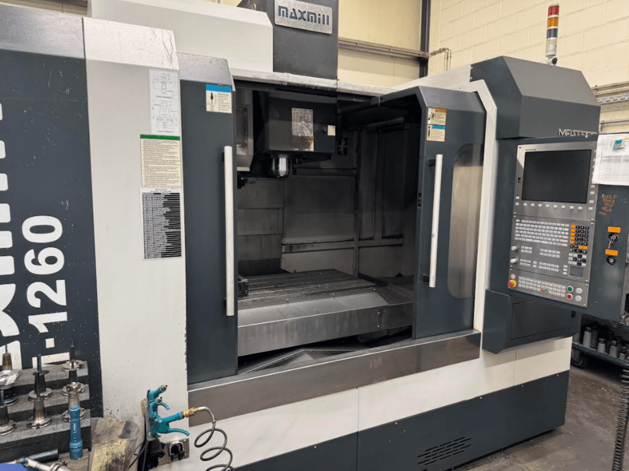 CNC frézka Maxmill, model M-1260, pohled zepředu na prázdný pracovní prostor s ovládacím panelem a návodem k obsluze.