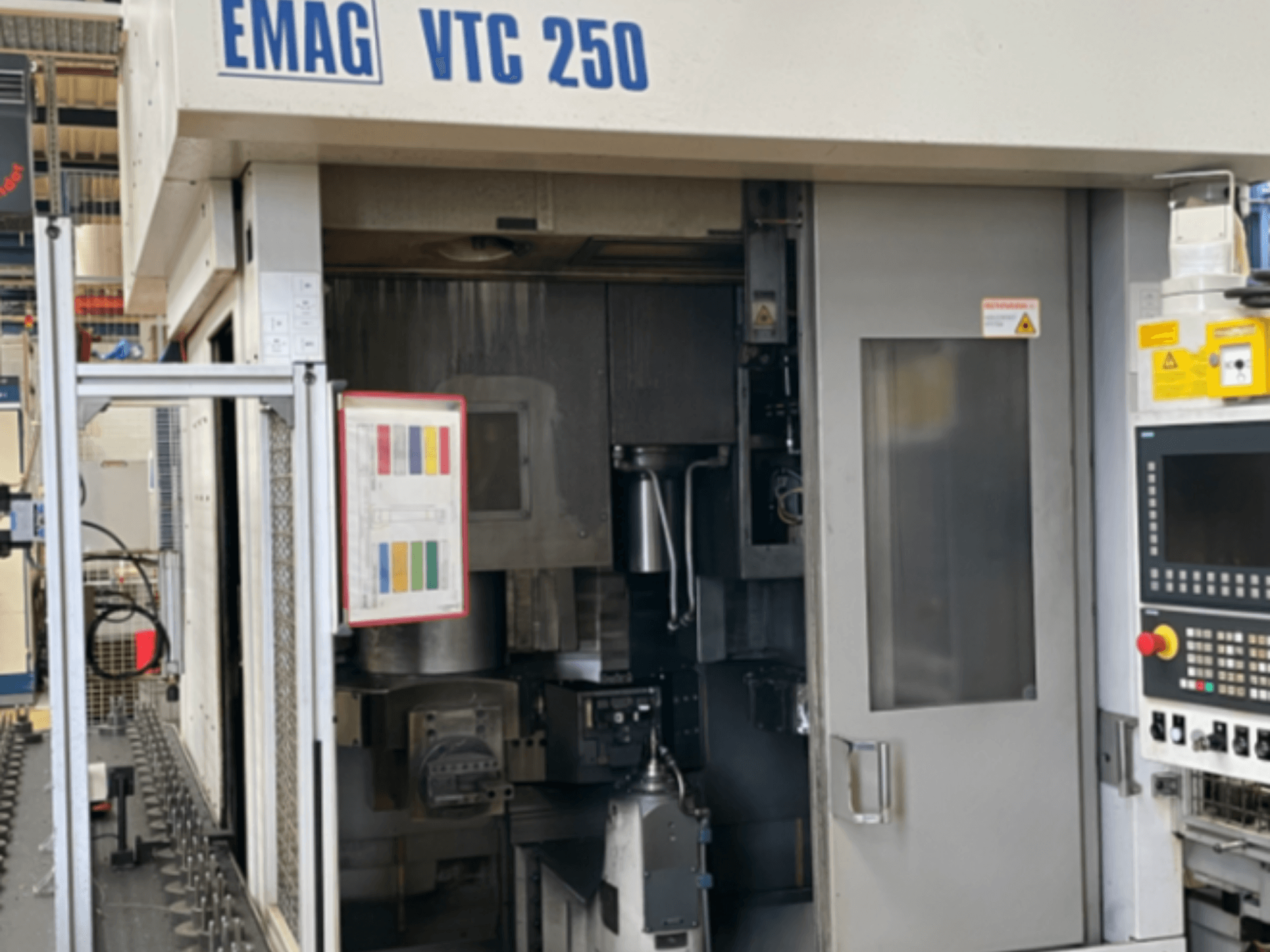 Pohled zepředu na vertikální soustruh EMAG VTC 250, na kterém je vidět ovládací panel, uživatelské rozhraní a otevřené přístupové dvířka.