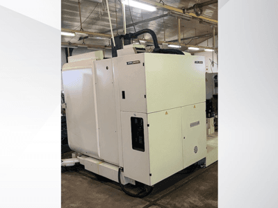 Bílý průmyslový CNC stroj při pohledu zepředu, s ovládacím panelem a ventilací, v dílenském prostředí.