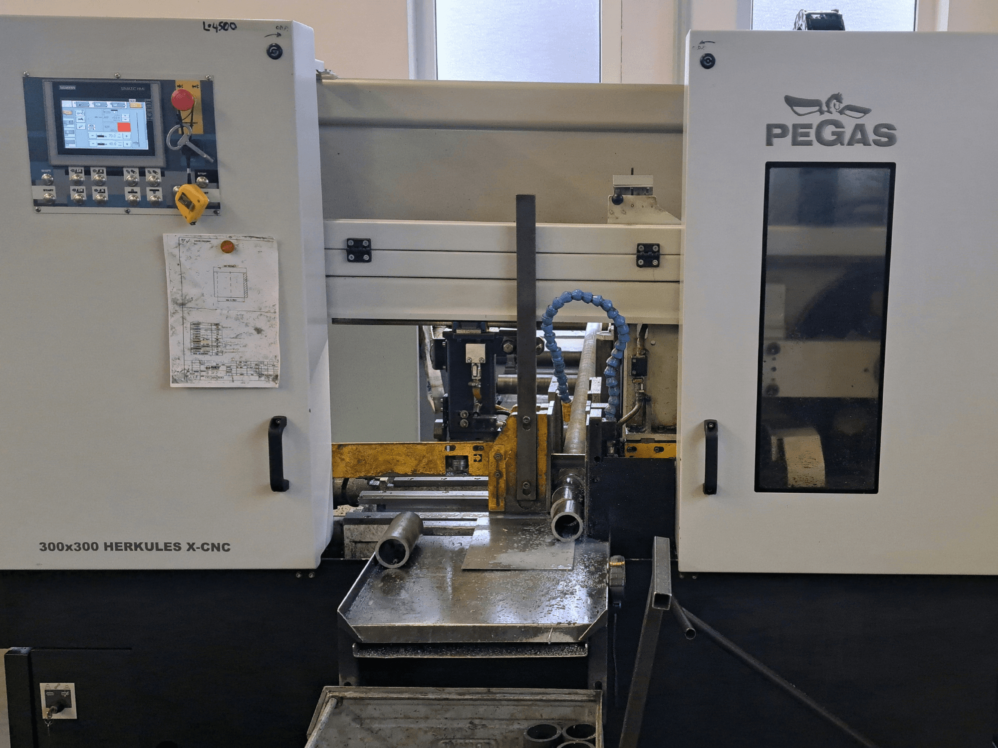 Stroj na zpracování plechu Pegas HERKULES X-CNC 300x300, pohled zepředu, na kterém je vidět ovládací panel a pracovní plocha s kovovými díly.