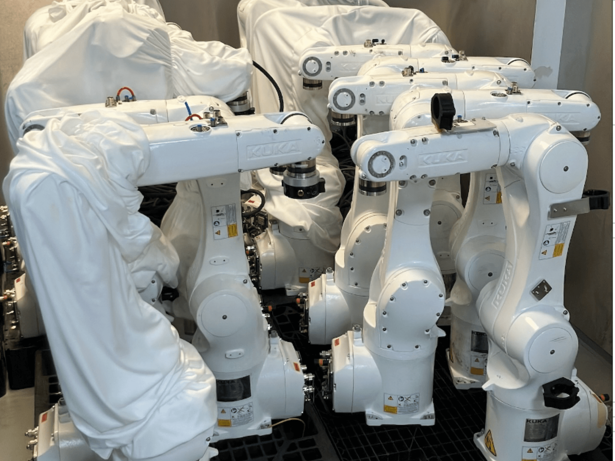 Robotická ramena KUKA KR 10 R900-2 potažená bílou látkou, pohled shora, ukazuje několik jednotek ve skladu.