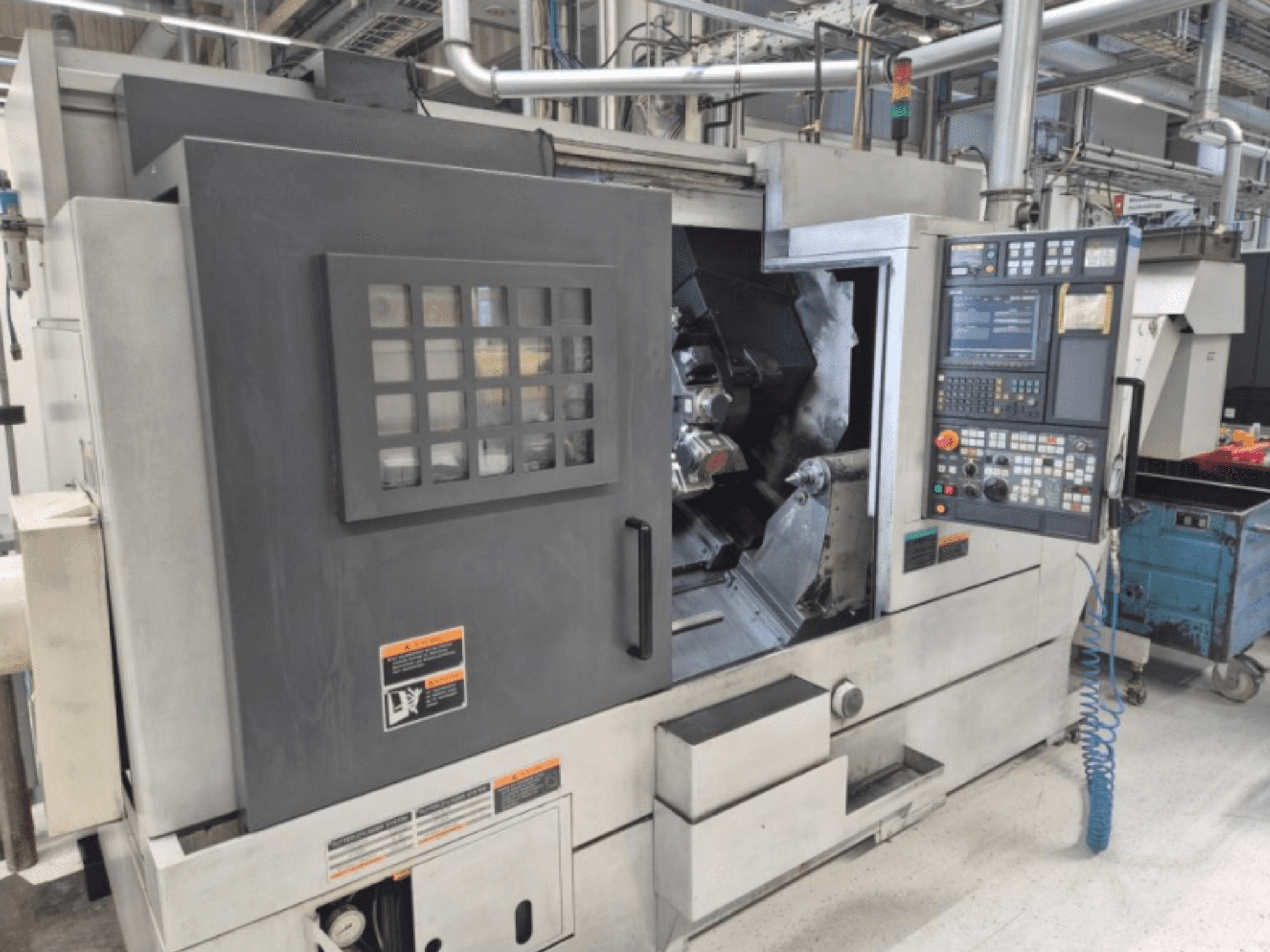 CNC soustruh s ovládacím panelem, pohled zepředu. Má viditelný pracovní prostor a bezpečnostní okénko, značka neznámá.