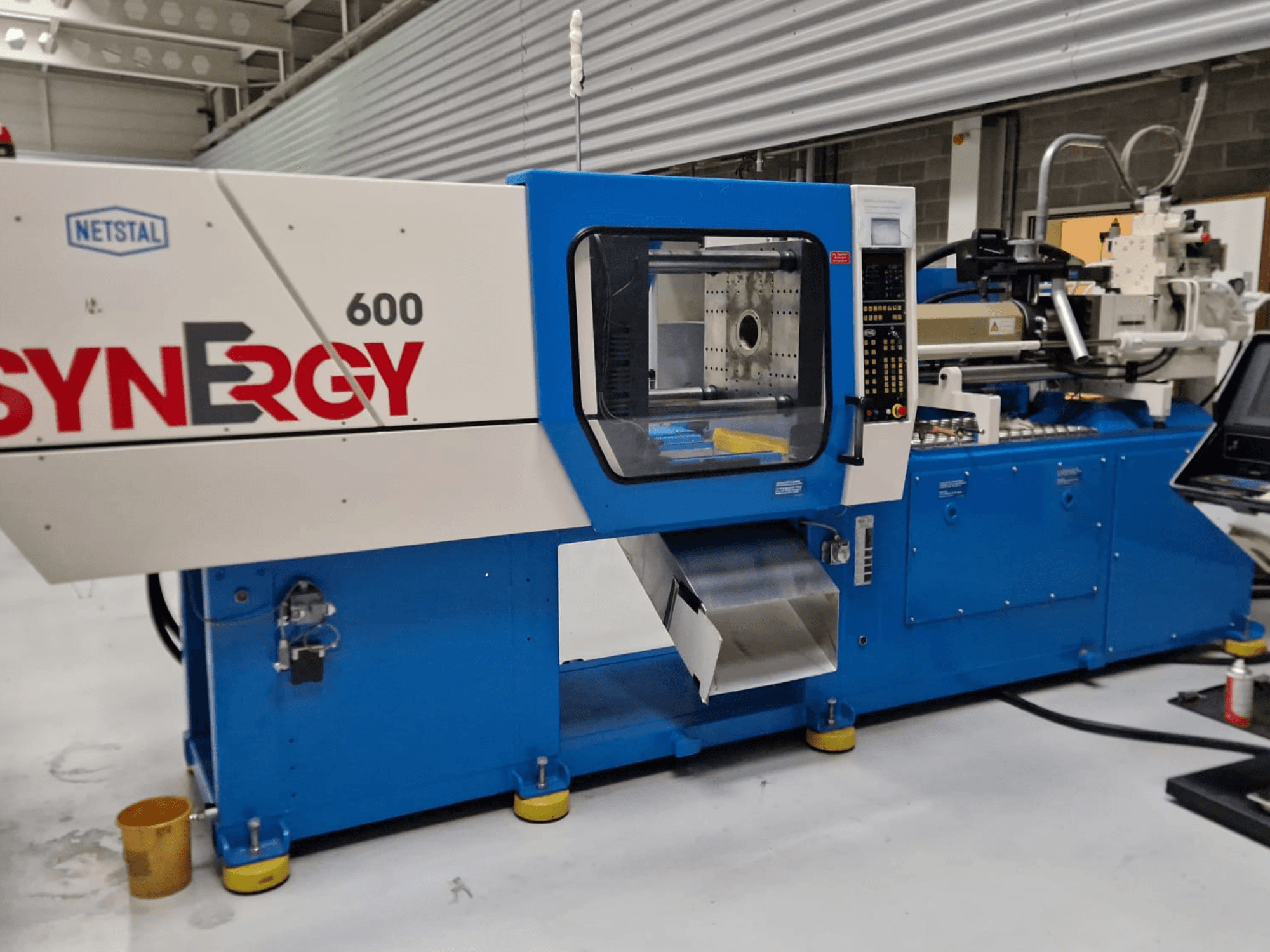 Hydraulický vstřikovací stroj Netstal Synergy 600-230, boční pohled na ovládací panel a vstřikovací prostor.