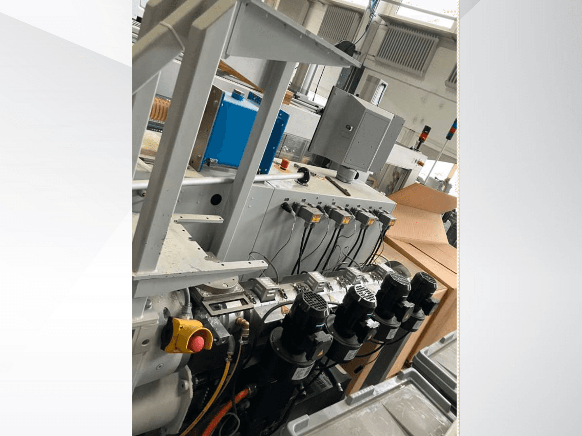 Ovládací panel průmyslových strojů s několika motory, měřicími přístroji a monitorem; pohled z boku v továrním prostředí.