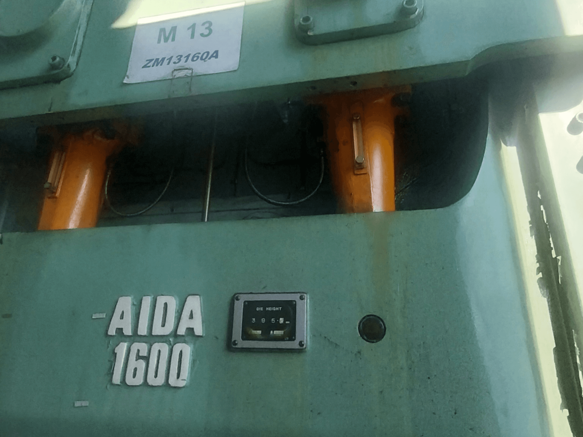 Mechanický lis AIDA NC2-1600, pohled zepředu; viditelné oranžové hydraulické komponenty a měřidlo výšky matrice.