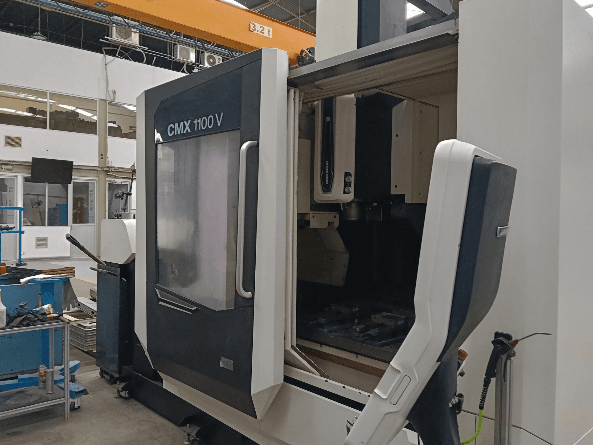 Vertikální obráběcí centrum DMG MORI CMX 1100 V, pohled zepředu s otevřenými dvířky a uspořádáním nástrojů v průmyslovém prostoru.