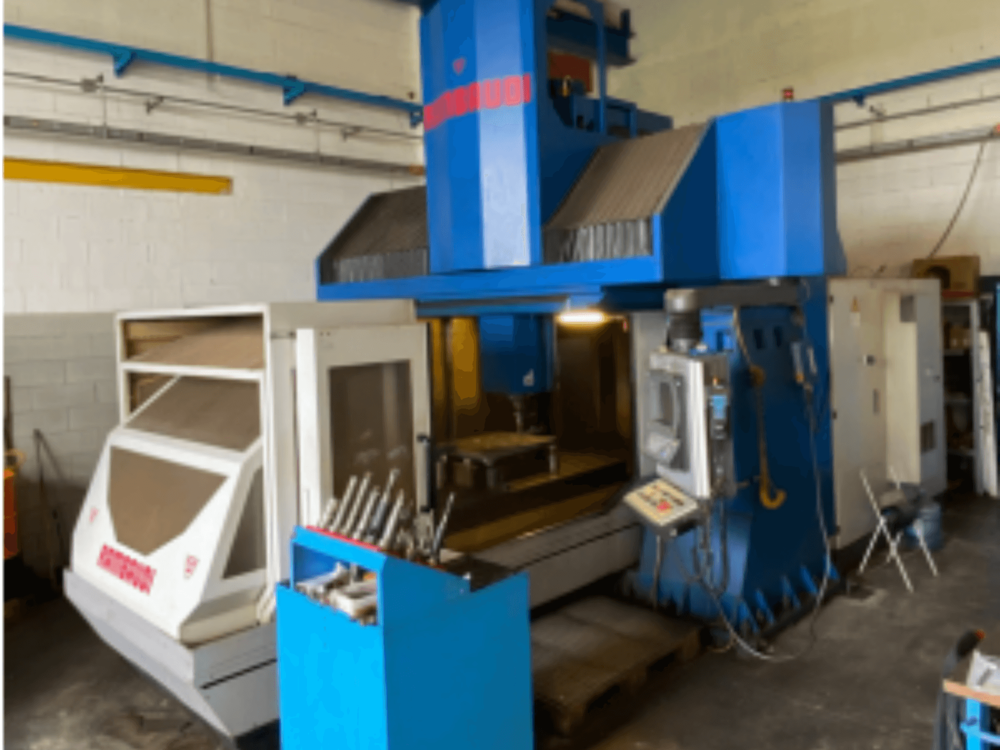 Vertikální obráběcí centrum Rambaudi RF103, čelní pohled zobrazující ovládací prvky, úložný prostor pro nástroje a obráběcí prostor. Modrobílý exteriér.