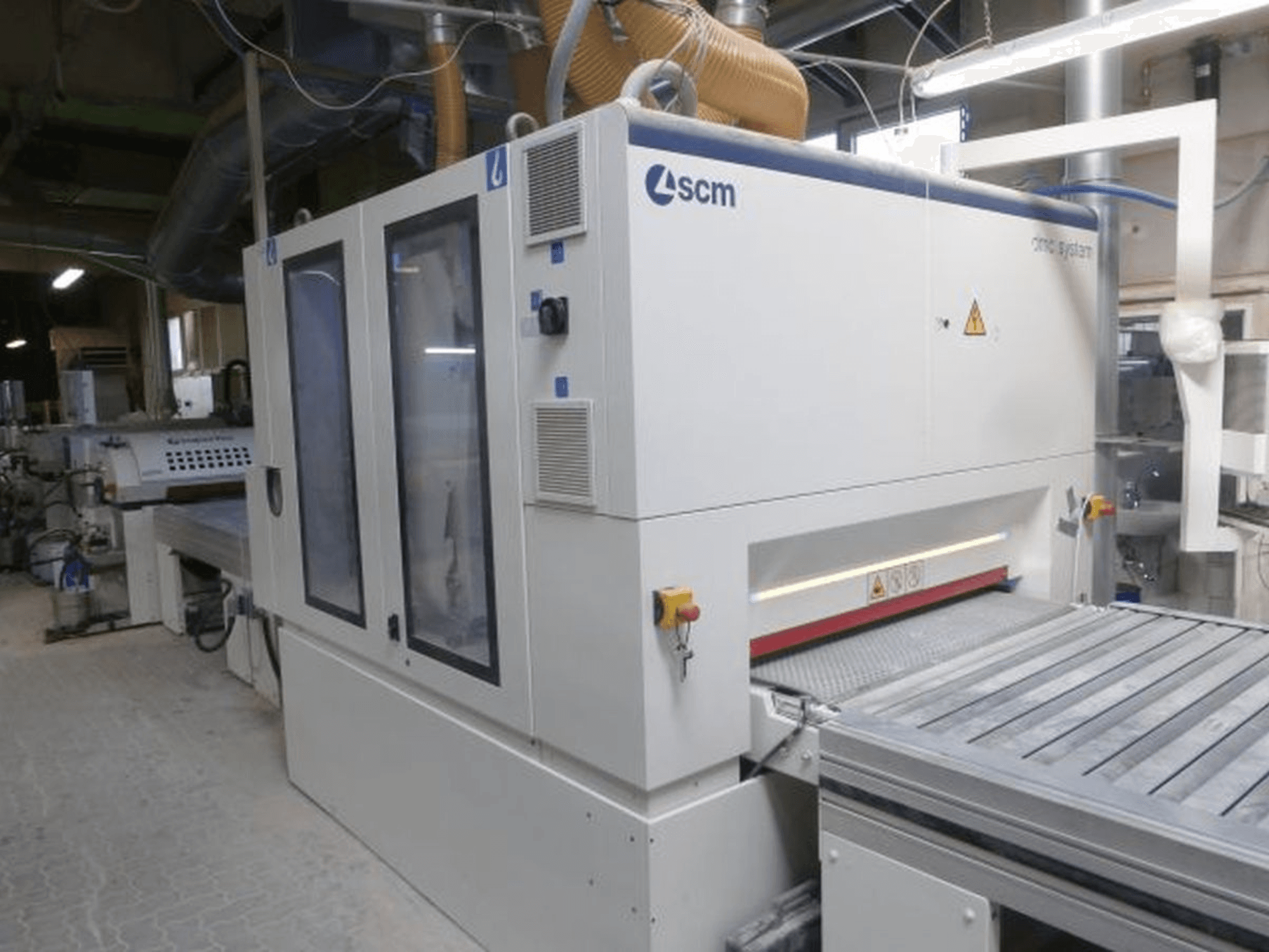 Pásová bruska SCM DMC SY TC 1350 v dílně, boční pohled znázorňující ovládací panel a brusnou plochu s bezpečnostními prvky.