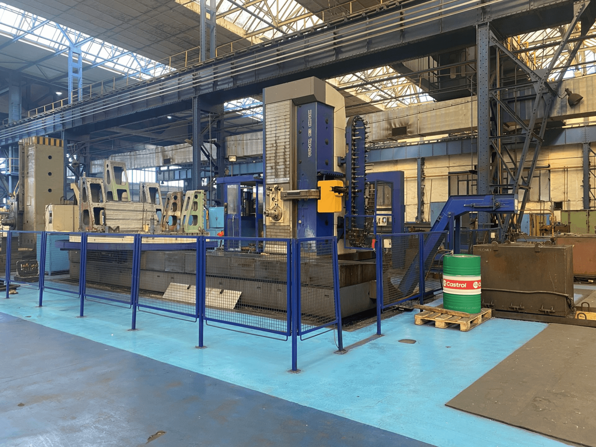 CNC vyvrtávačka TOS WHQ 13 v dílně, pohled zepředu, modrý rám a okolní bezpečnostní oplocení.