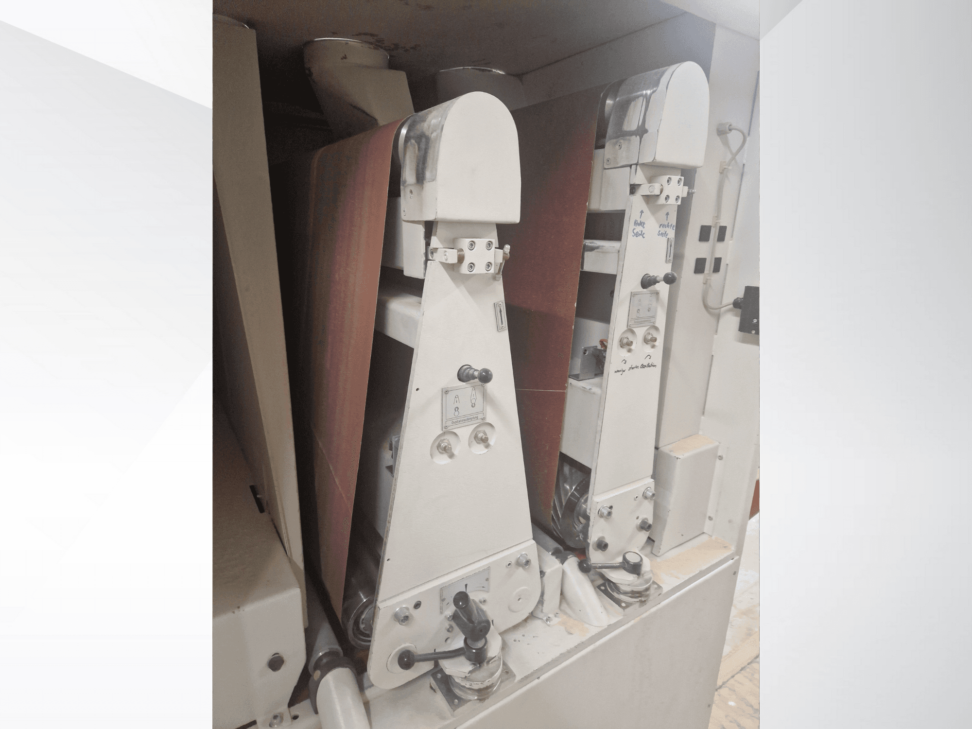 Dva průmyslové brusné stroje s červenými brusnými pásy, pohled zepředu, ovládací prvky a kovové součásti.