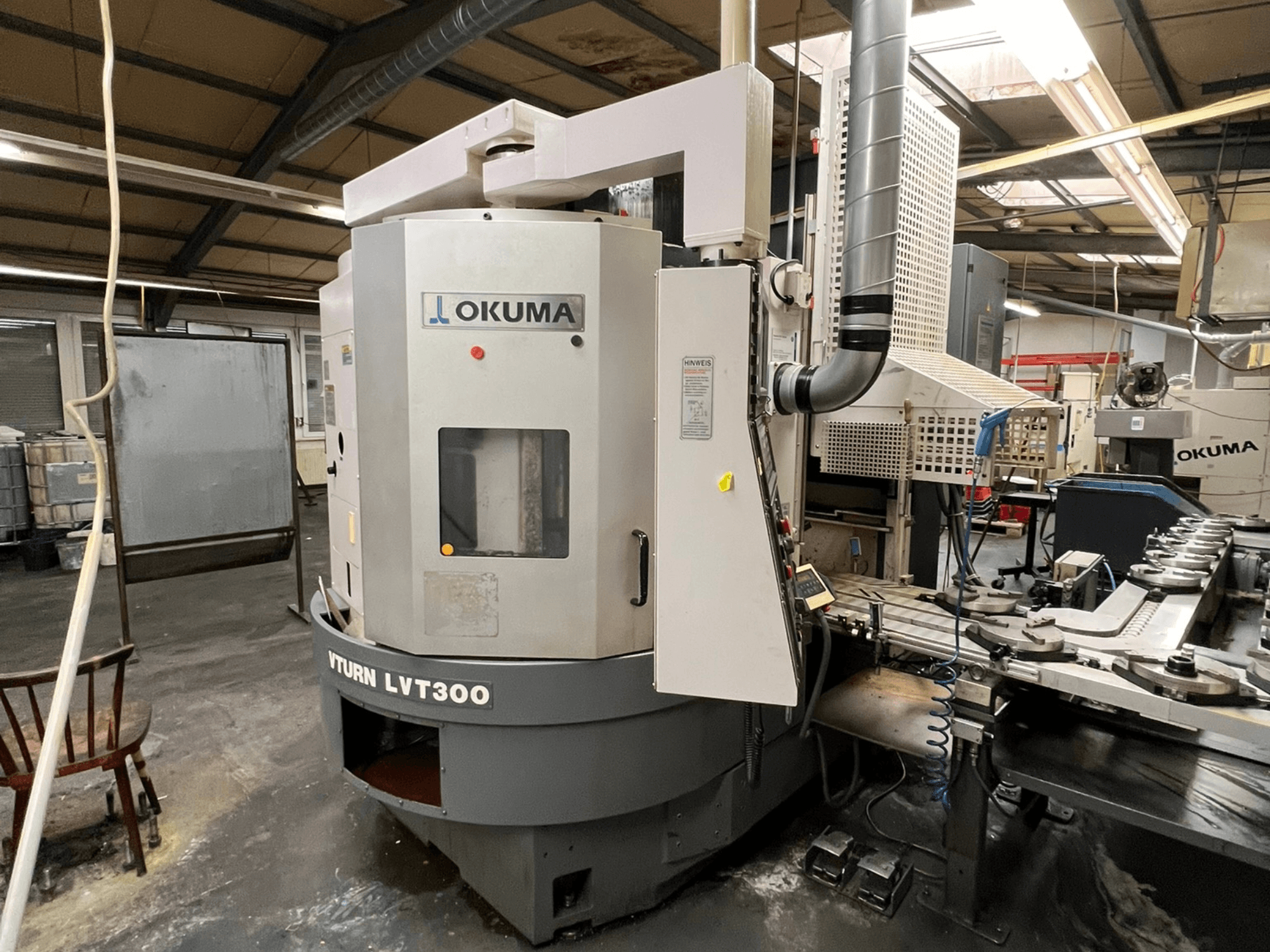 CNC soustruh Okuma Vturn LVT300, boční pohled v průmyslovém prostředí, ukázka ovládacího panelu a chladicího systému.